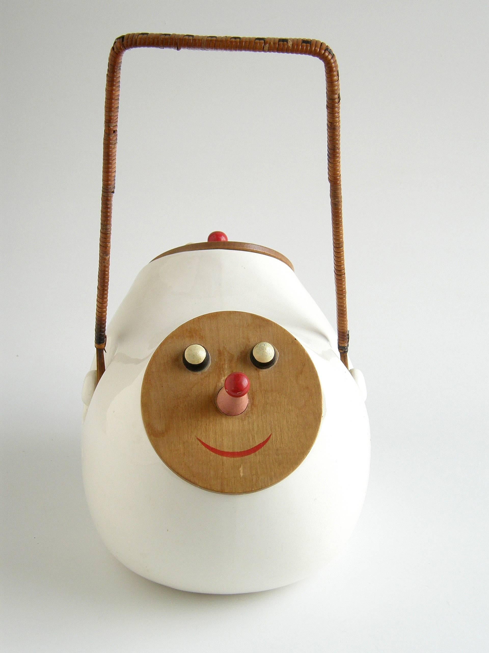 This amusing ceramic cookie jar designed by Lagardo Tackett has an opening on each side. The lids of the two openings are made of wood and painted with clownish, smiling faces. Their red-tipped pink noses form their handles. The tall, woven rattan