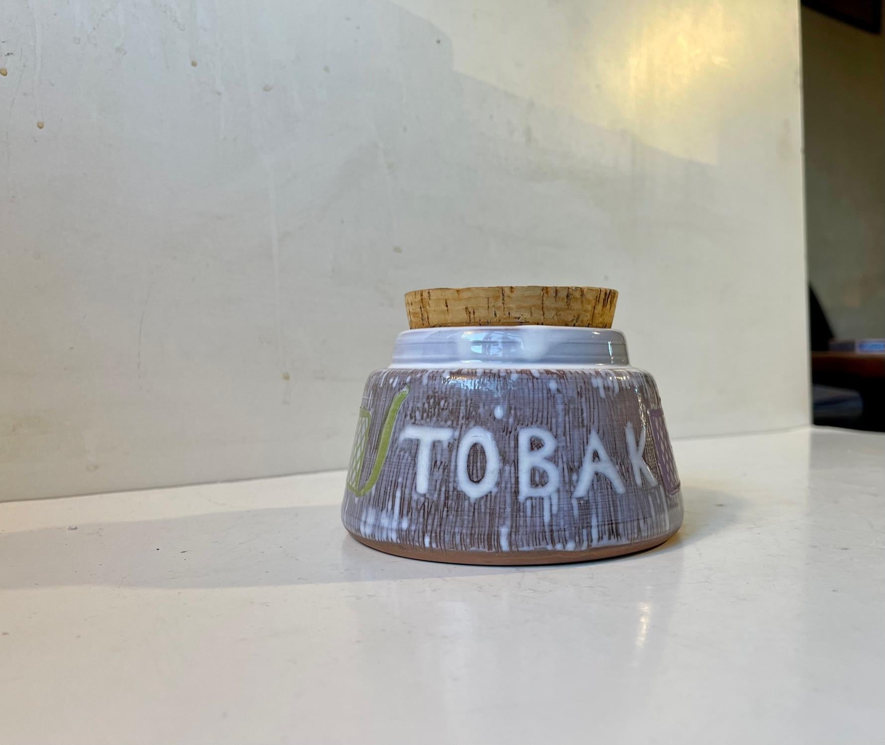 Sgrafitto decorated pipe tobacco humidor from Laholm Studio in Sweden. Polychrome glazes: purple, white, green, brown. Feturing its original cork lid. Signed/marked. Made circa 1960-65. Measurements: H: 9 cm, D: 12 cm.