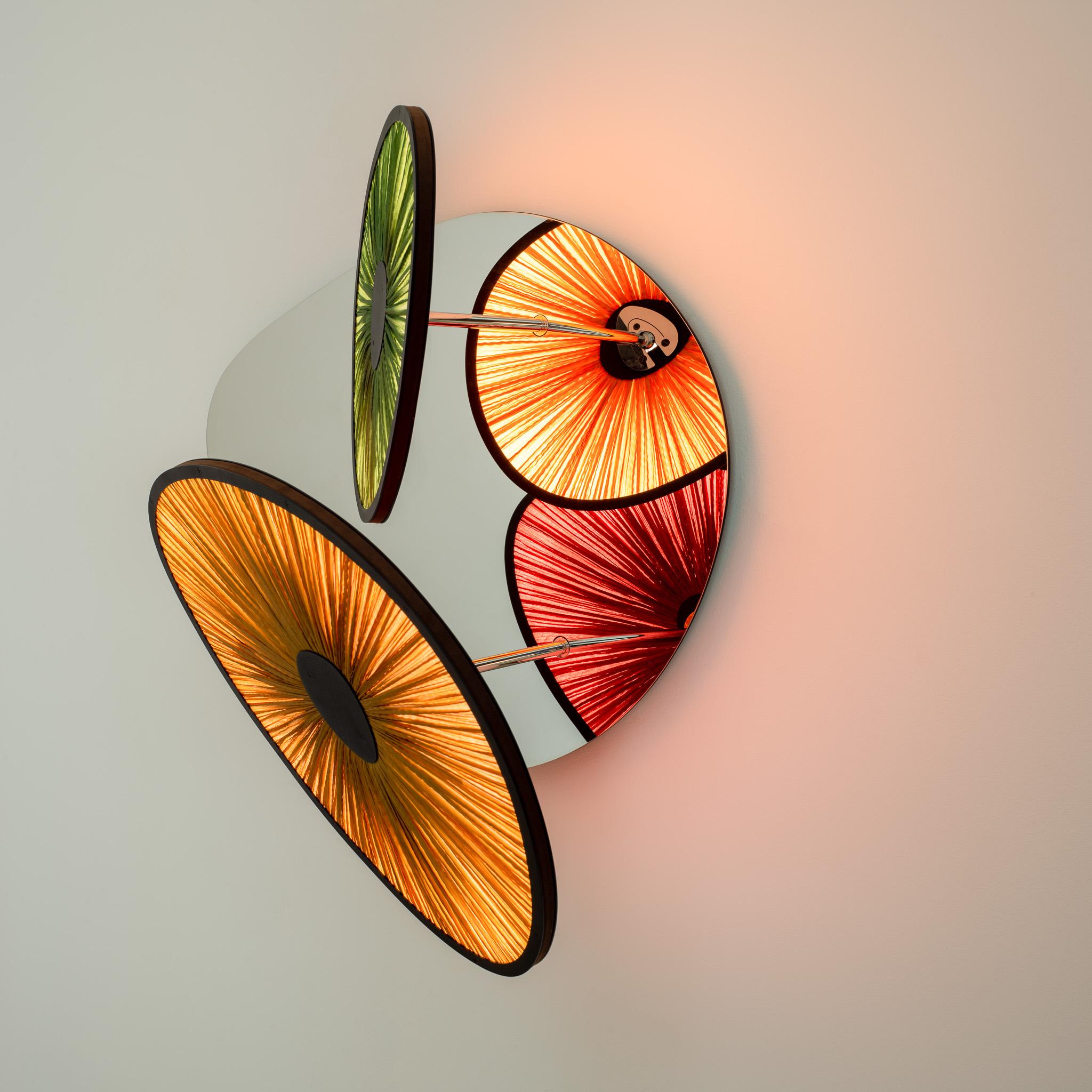 The Lake Doiran Mirror Wall Light (2 Lights) is a unique and innovative design by Albi Serfaty. This lamp features the studio's latest technology and explores the play of light and color with its multi-colored silk shades that can move individually