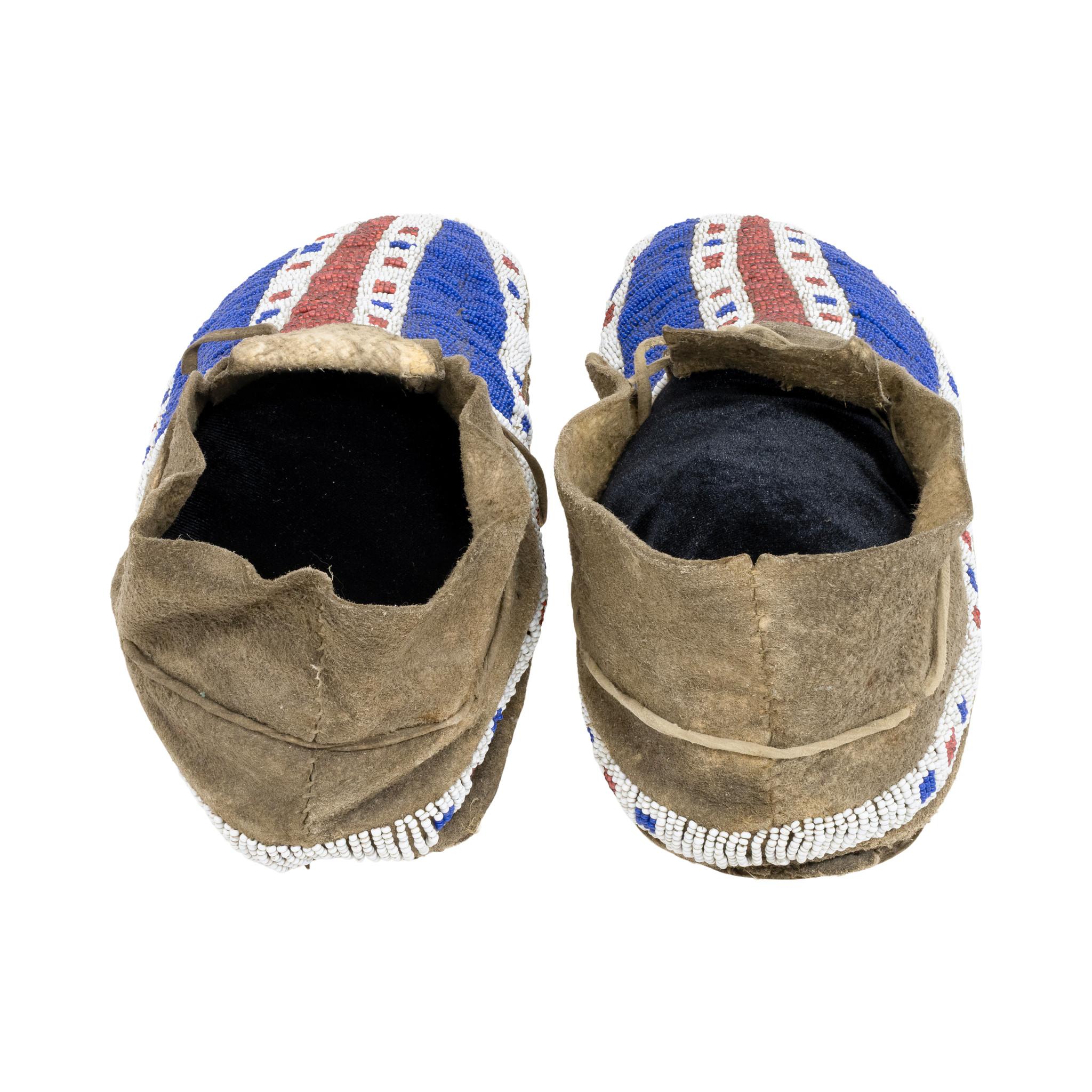 Lakota Sioux moccasins with buffalo hoof motif. Red white heart beads and brain tanned hide with hard soles. Sinew sewn, soft hide. Right moccasins has a partial old collection paper glued to sole. Left moccasin's sole has water damage from period