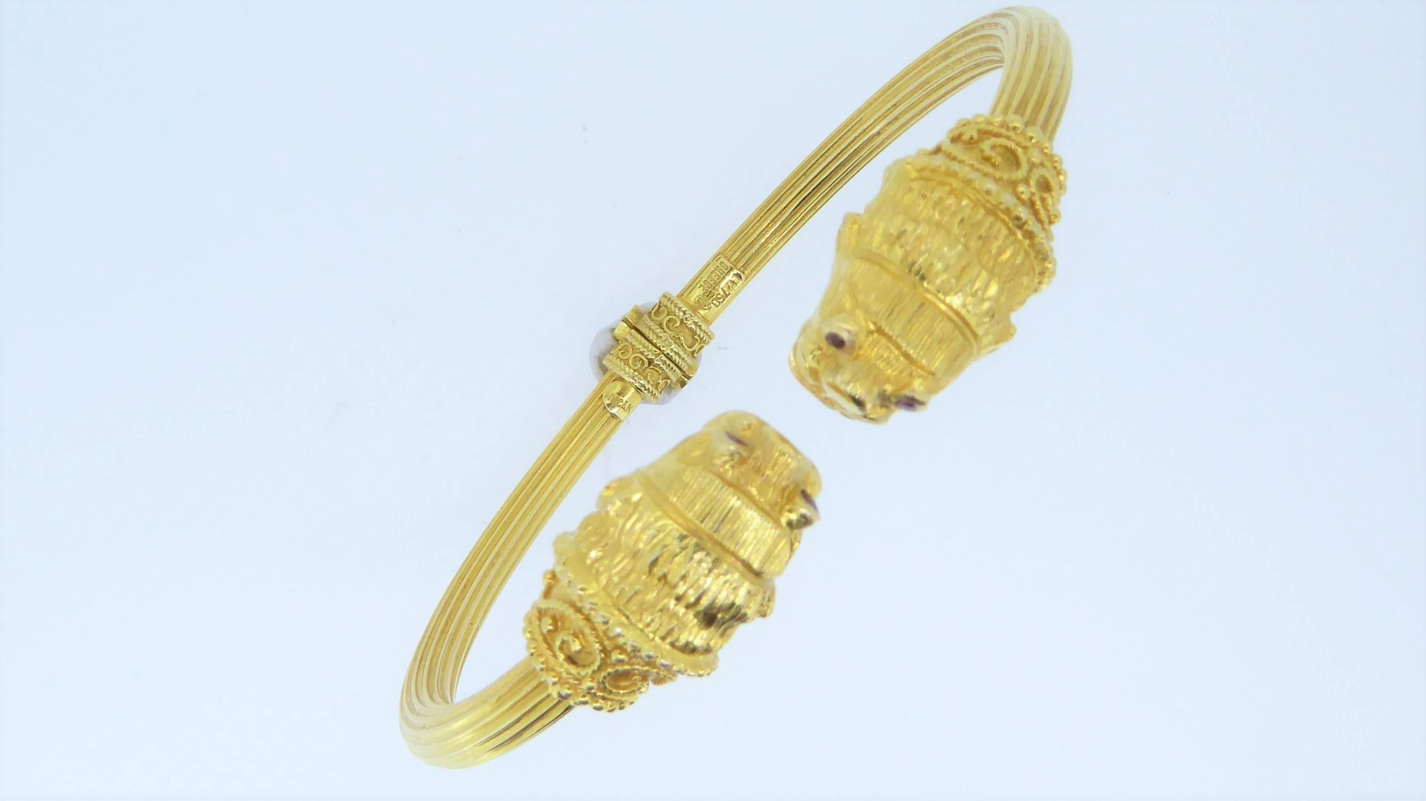 A Lalaounis 18 Carat Yellow Gold Double-Headed Lion Bangle. The hinged, reeded bangle with lion-head terminals and reuby-set eyes. Circa 1980. Stamped 