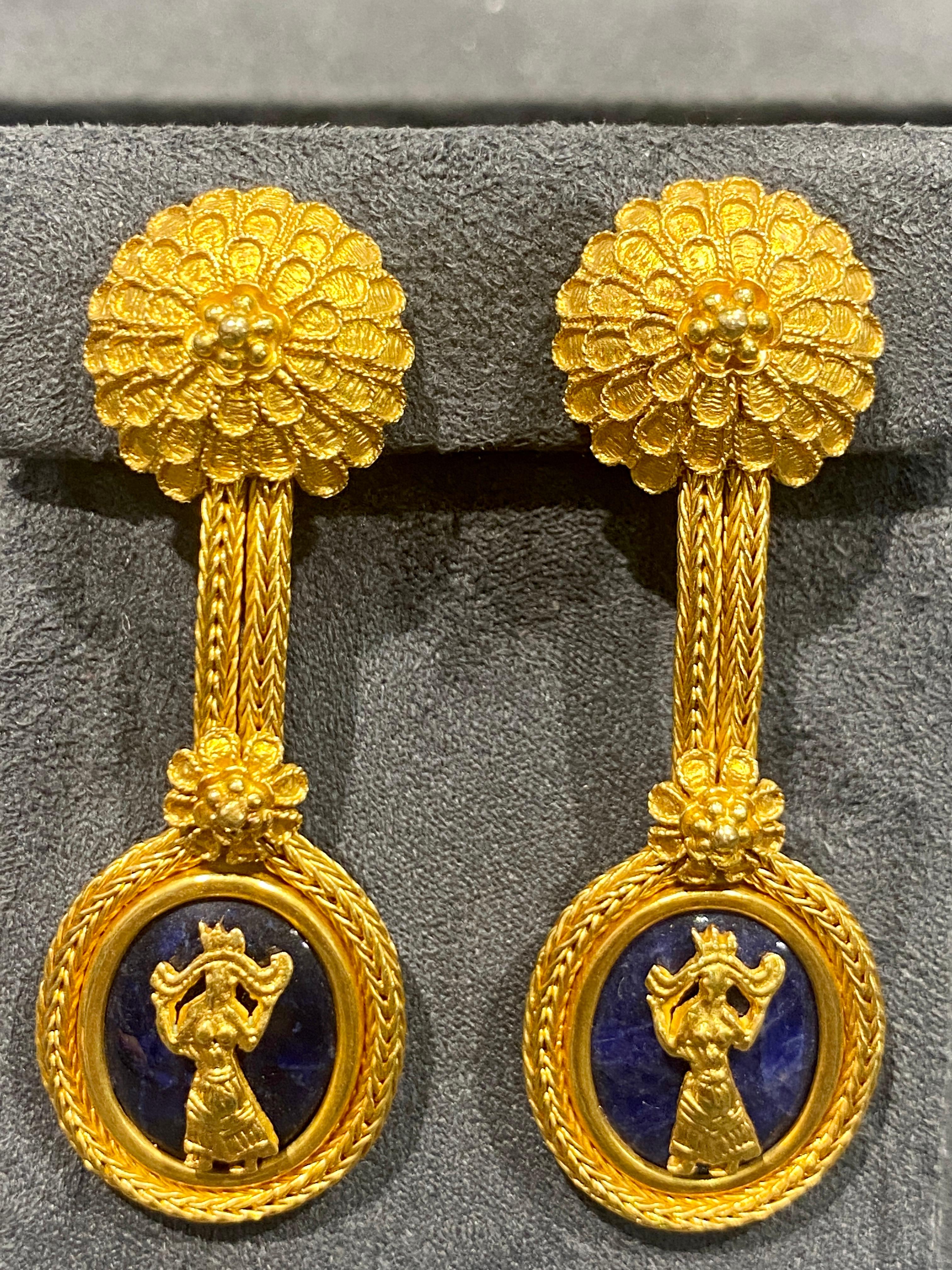 These impressive 18k gold Lalaounis clip-on dangly earrings are classical in design. The top of the earring that rests on the earlobe is an intricate floral pattern while at the bottom there is a vignette of a golden female figure on an oval shaped