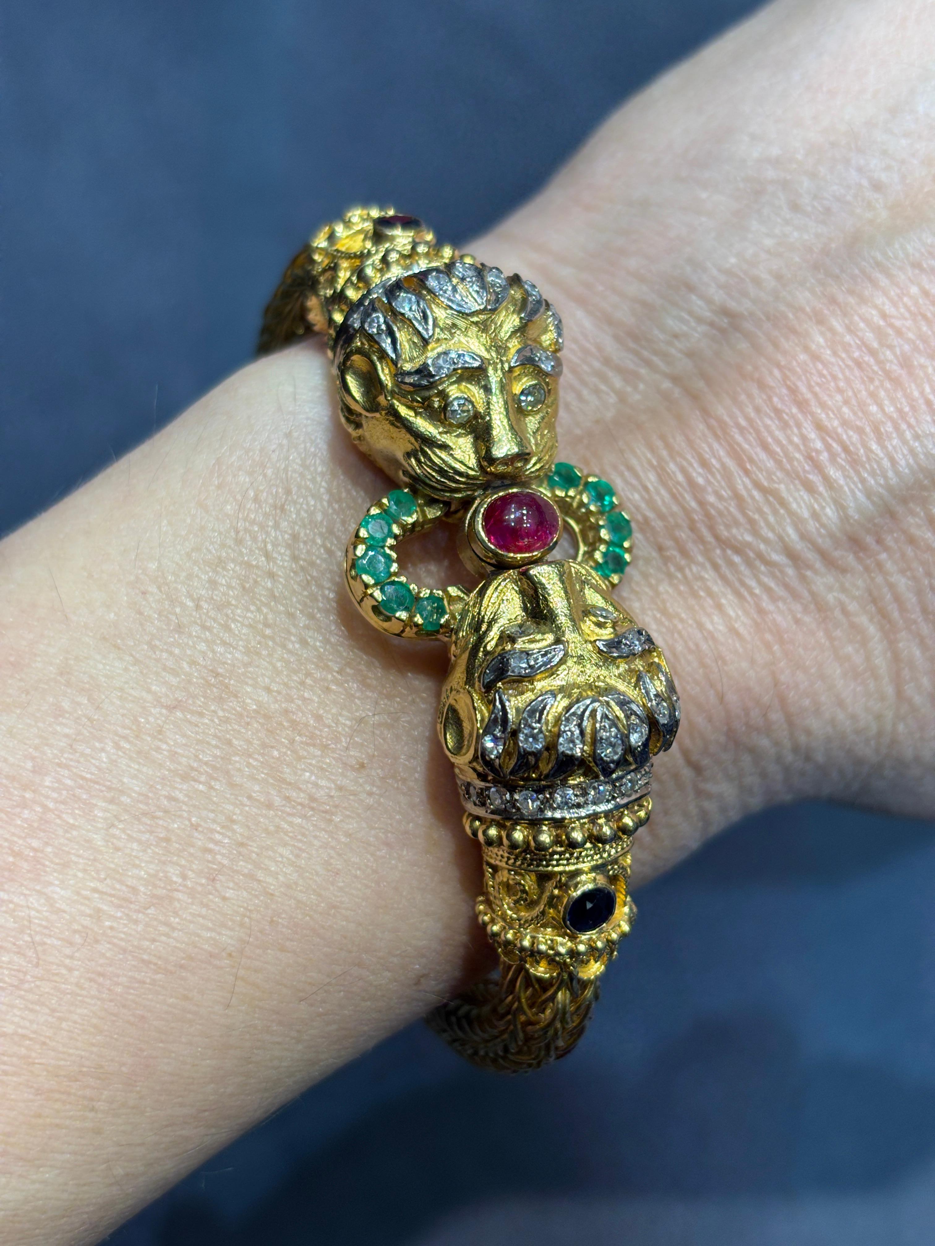 This intricately made Ilias Lalaounis bangle from 1980s is in the shape of 2 lion's heads joined by a cabochon ruby. The bangle is beautifully made in 18k gold and adorned with diamonds, sapphires and emeralds. Its circumference measures 18cm.