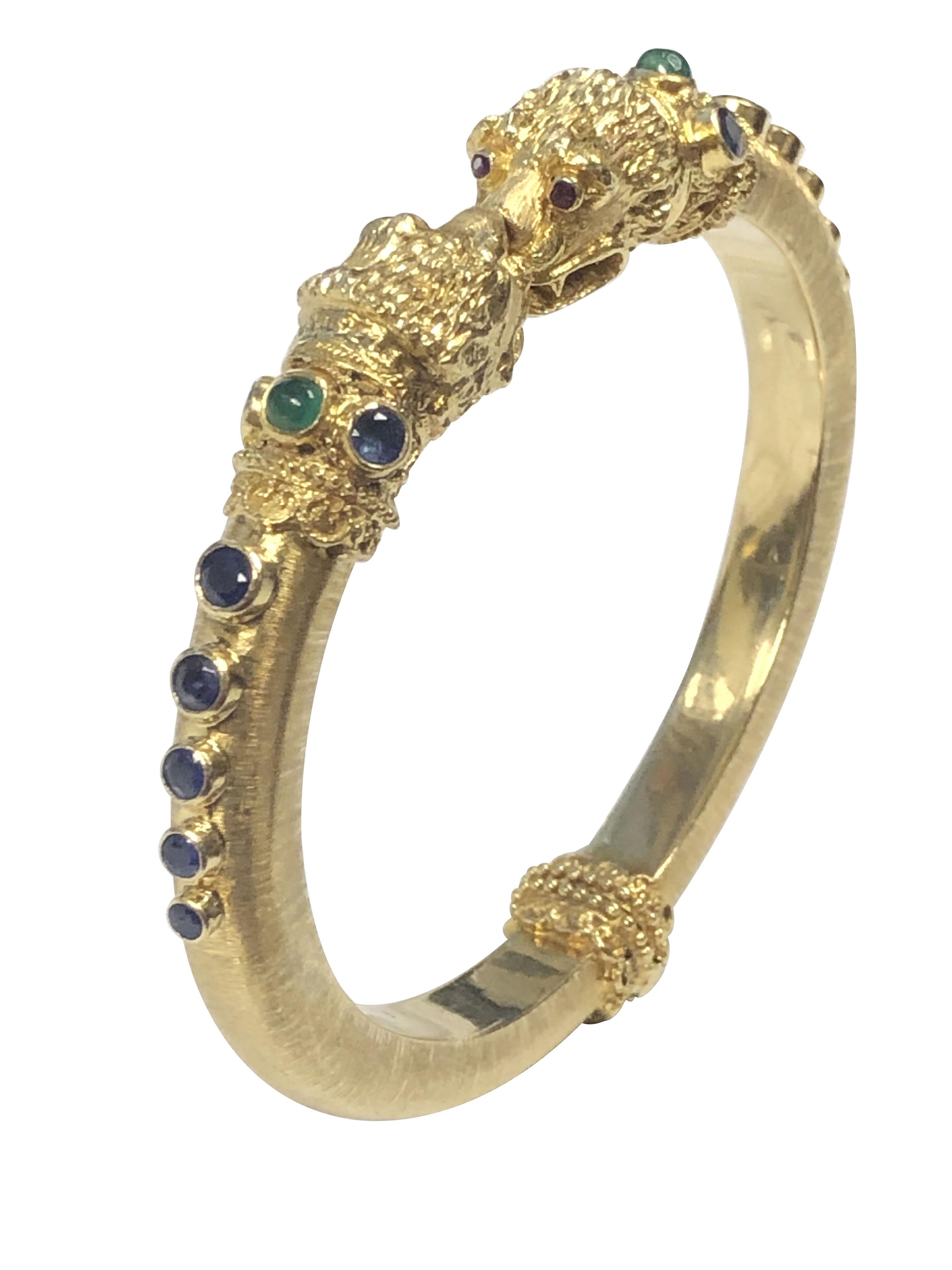 Circa 2000 Ilias Lalaounis Chimera Head hinged bangle Bracelet, 18K Yellow Gold and measuring 7 M.M. wide and weighing 44 Grams. with a light brushed finish,  finely detailed Chimera Heads and set with Cabochon Emeralds, Faceted Sapphires and Ruby