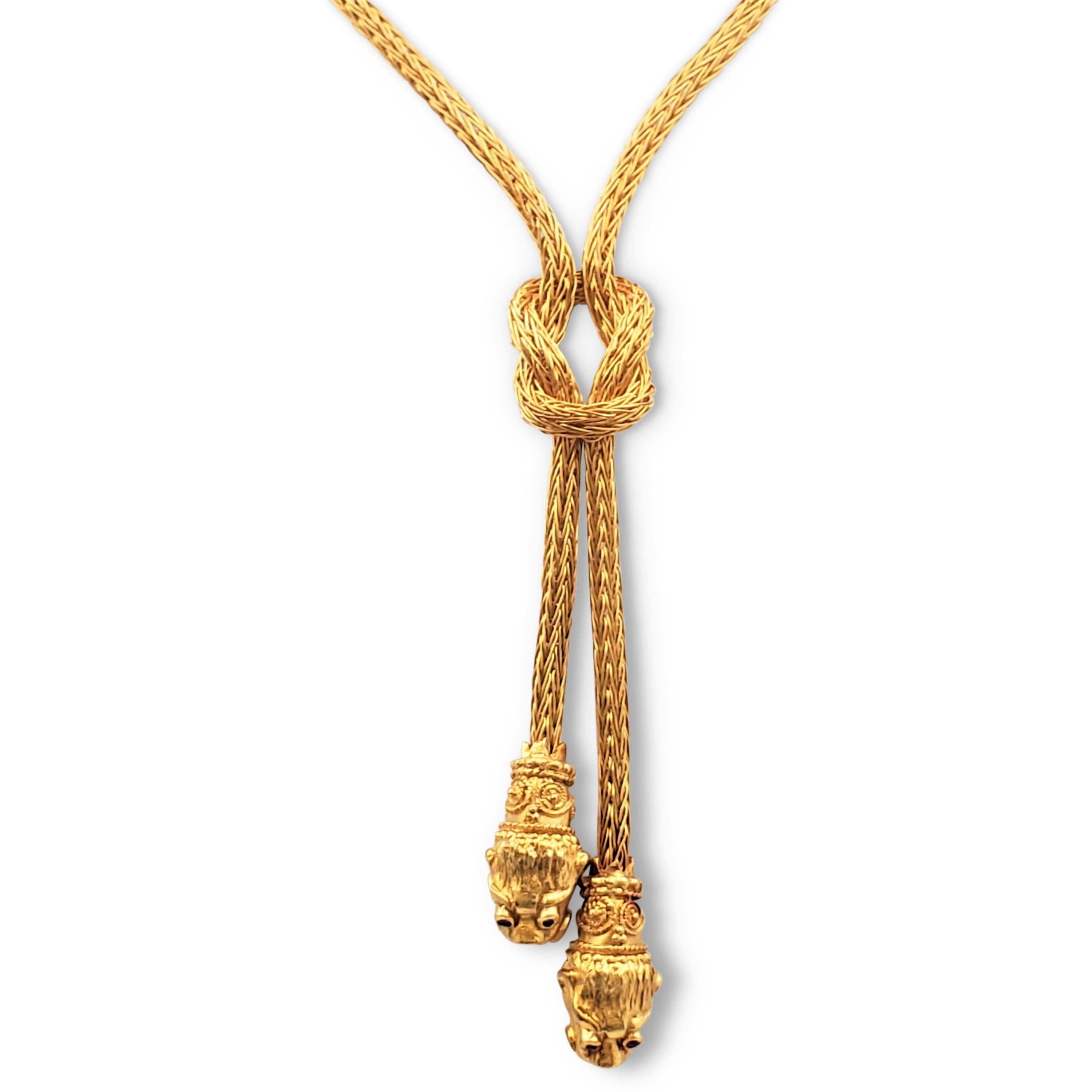 Authentic Ilias Lalaounis lariat necklace crafted in tubular braided 18 karat yellow gold centering a double knot, terminating in two stylized textured gold lion heads accented by ruby eyes. Patina consistent with age and wear. Lalaounis maker's