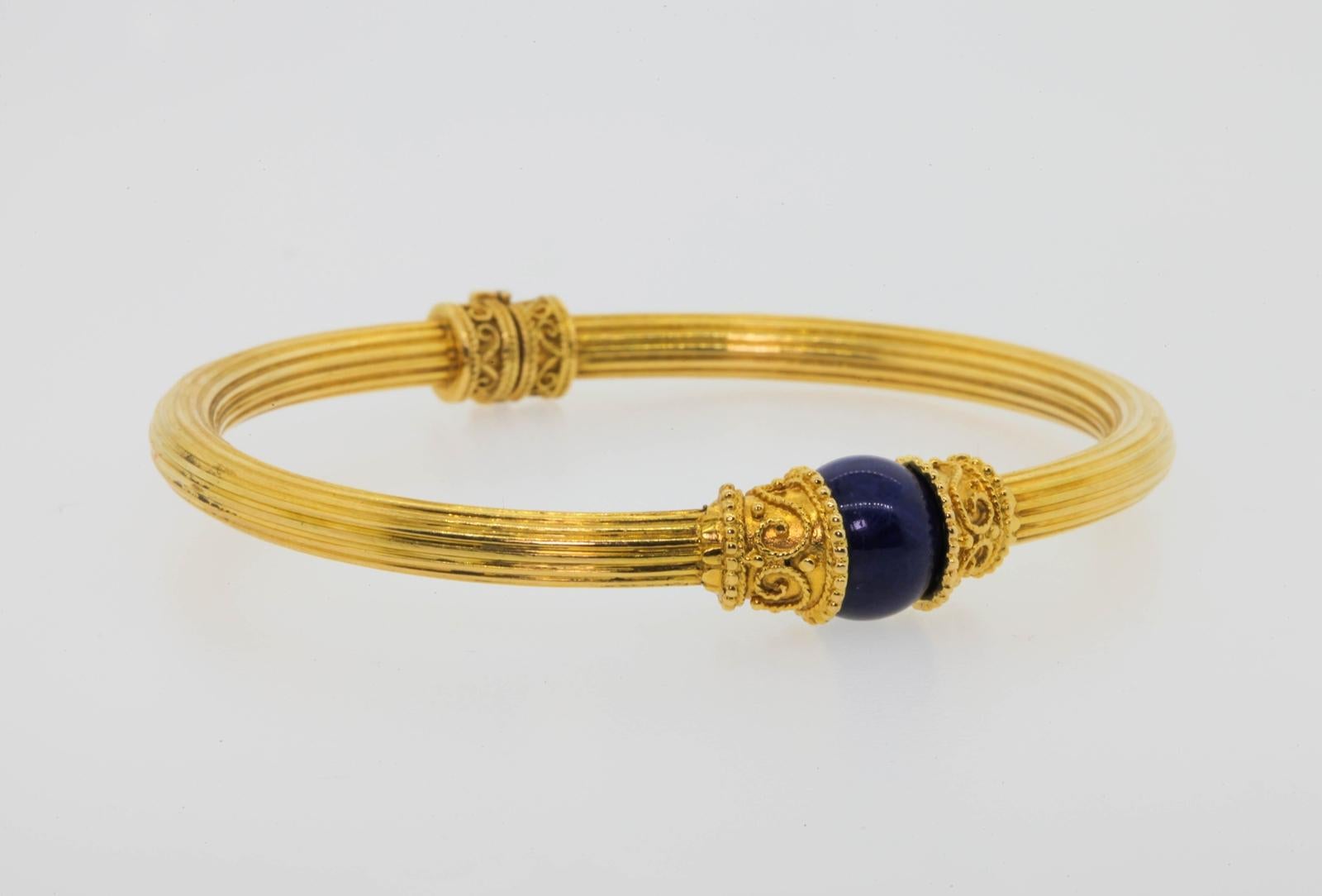 From Greece's most renowned jeweler Ilias Lalaounis this beautiful bangle bracelet.  The 18KT gold bangle features a fluted all around Lapis Azuli bead measuring 10.15 mm, hugged by beaded and rope like caps.   Two similiar bands adorn the hinge of