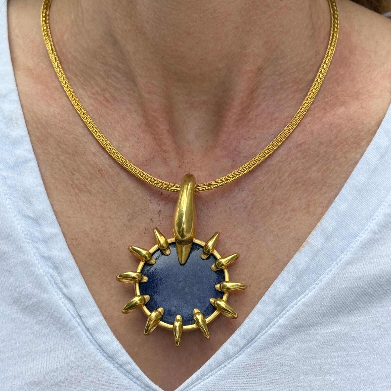 The Lalaounis Sodalite Swan 21 Karat Yellow Gold Disc Pendant Necklace is a sophisticated and artistic piece of jewelry. Featuring a striking disc pendant crafted from luxurious 21 karat yellow gold, the pendant showcases a detailed swan design with