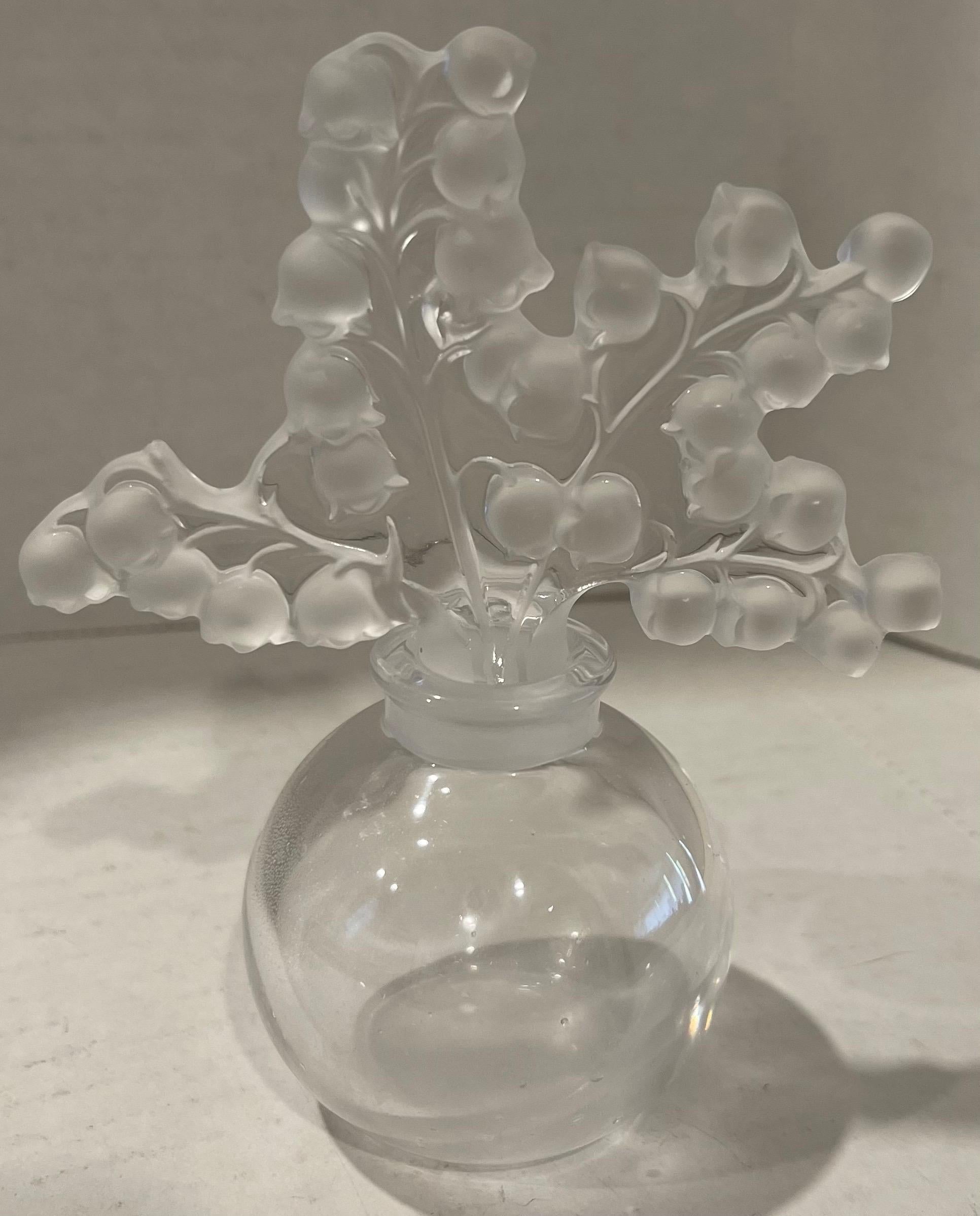 Profumo Lalique Clairefontaine mughetto anni '90. Corpo in vetro trasparente con tappo a fiore in vetro smerigliato. Firmato Lalique nella parte inferiore. 