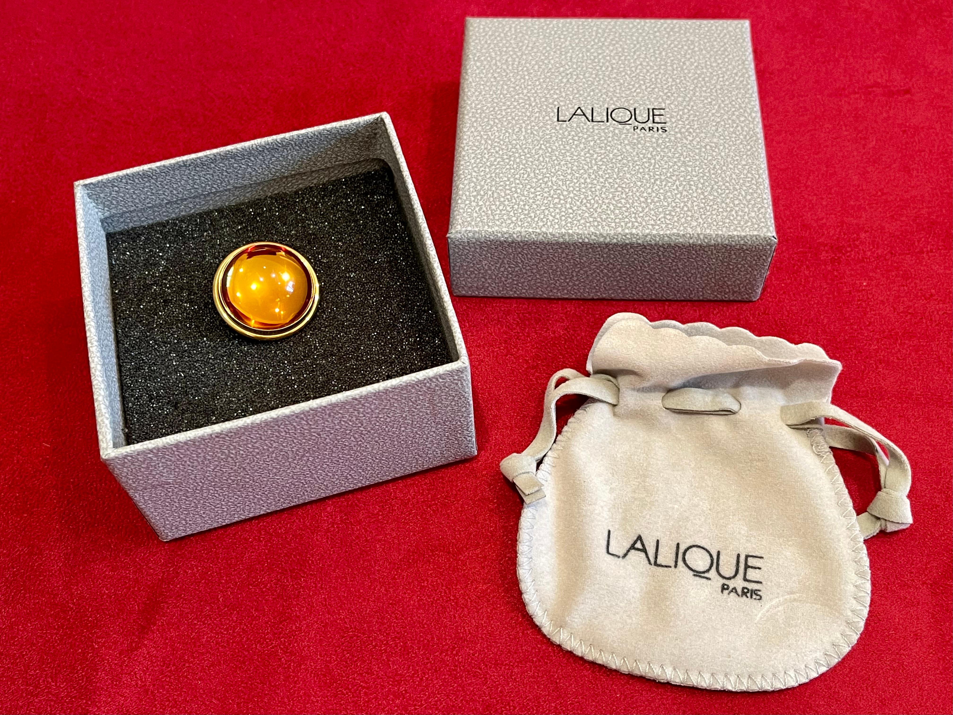 Broche en cristal de Lalique de couleur ocre formant un cabochon. Cadre en métal doré, épingles attachées. Boîte et certificat d'origine.
Dimensions - diamètre 2,5cm.