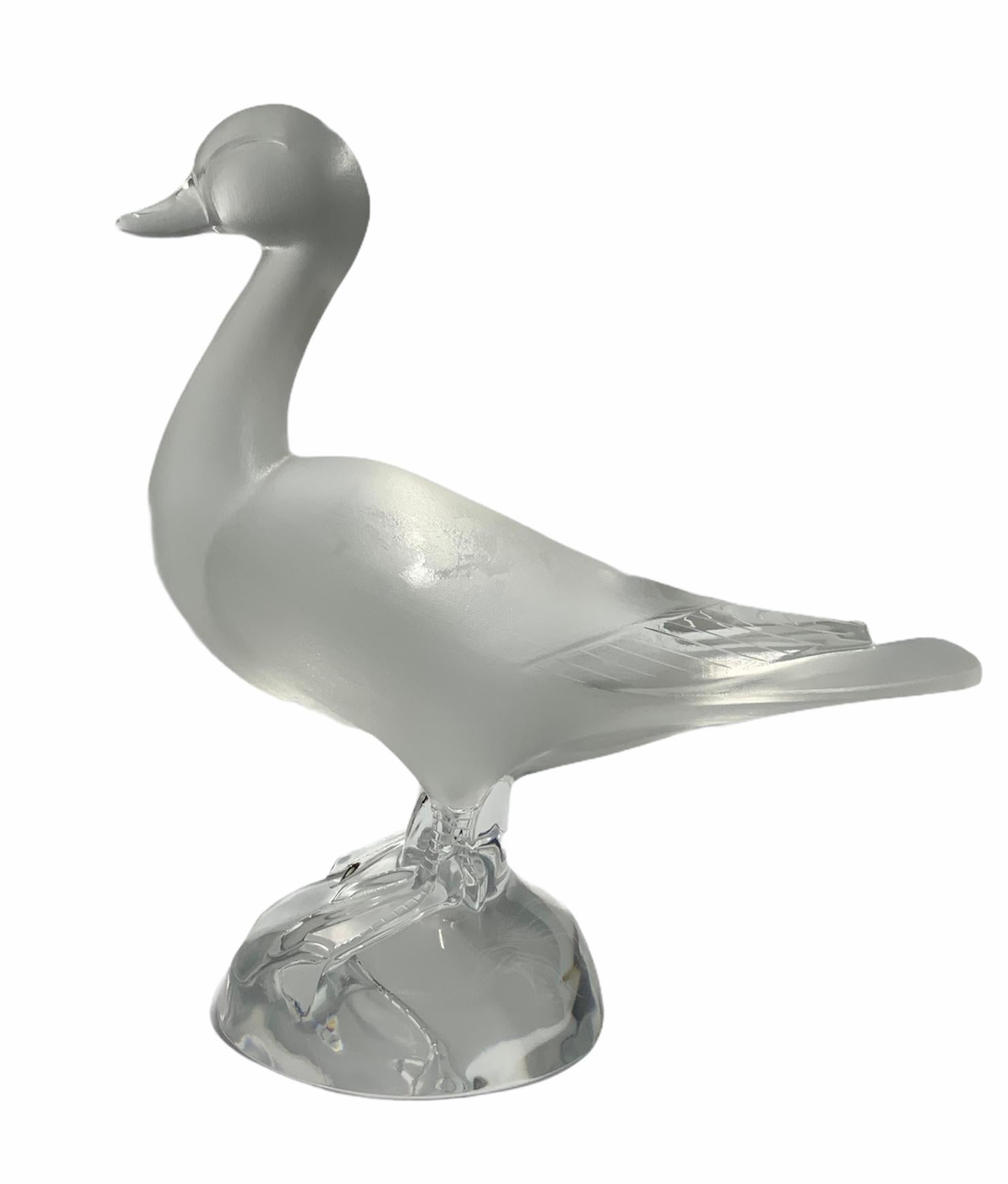 This is a Lalique Crystal frosted and clear glass sculpture of a charming duck. The sculpture is standing up over a round crystal base. It is signed Lalique, encircled R, France in the border of the base.