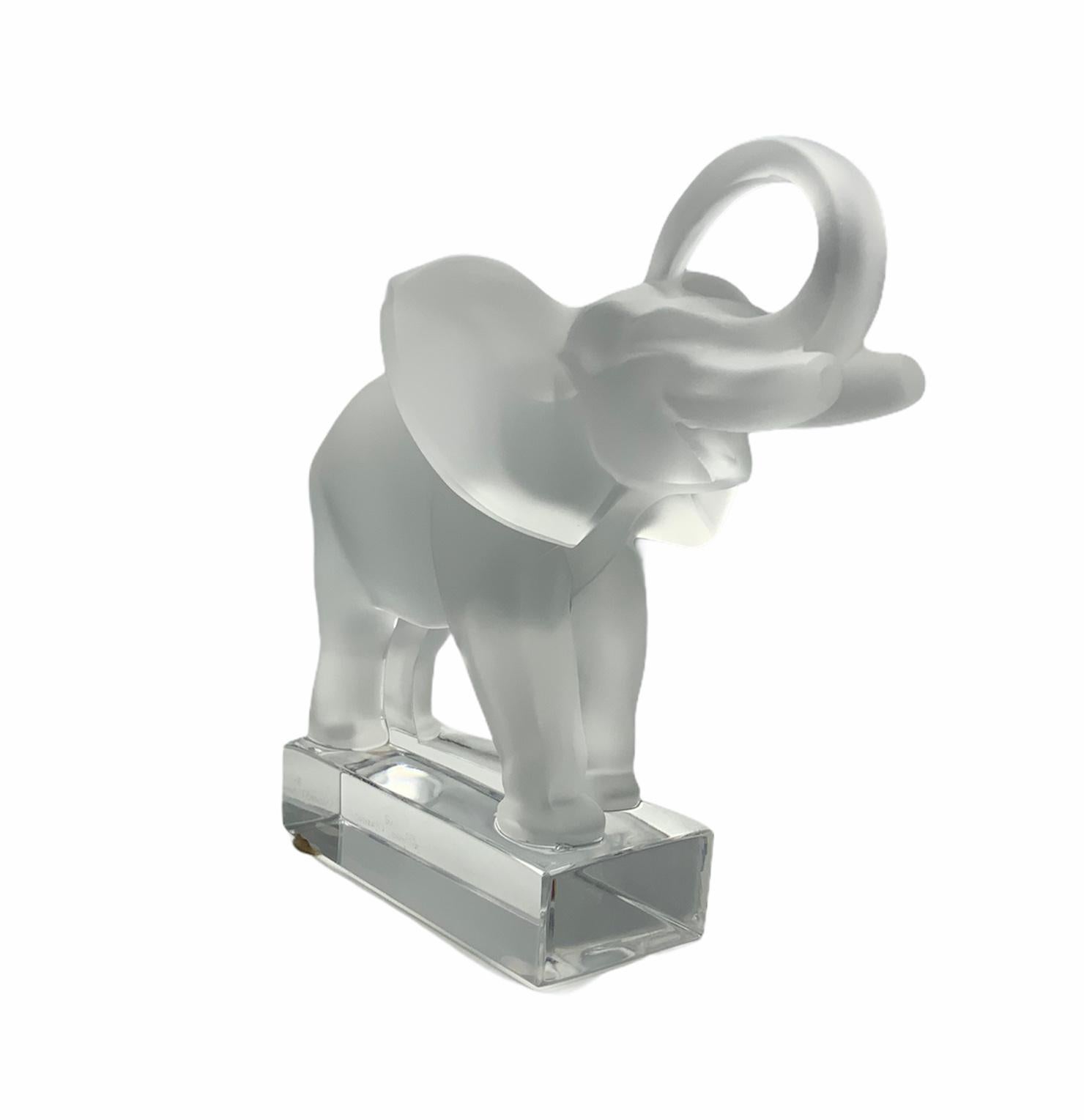 This is a Lalique frosted crystal sculpture of a happy elephant with a large trunk up. He is supported by a clear crystal rectangular base. In one of the border of the base is signed Lalique R France. Elephants are symbol of good luck, wisdom and
