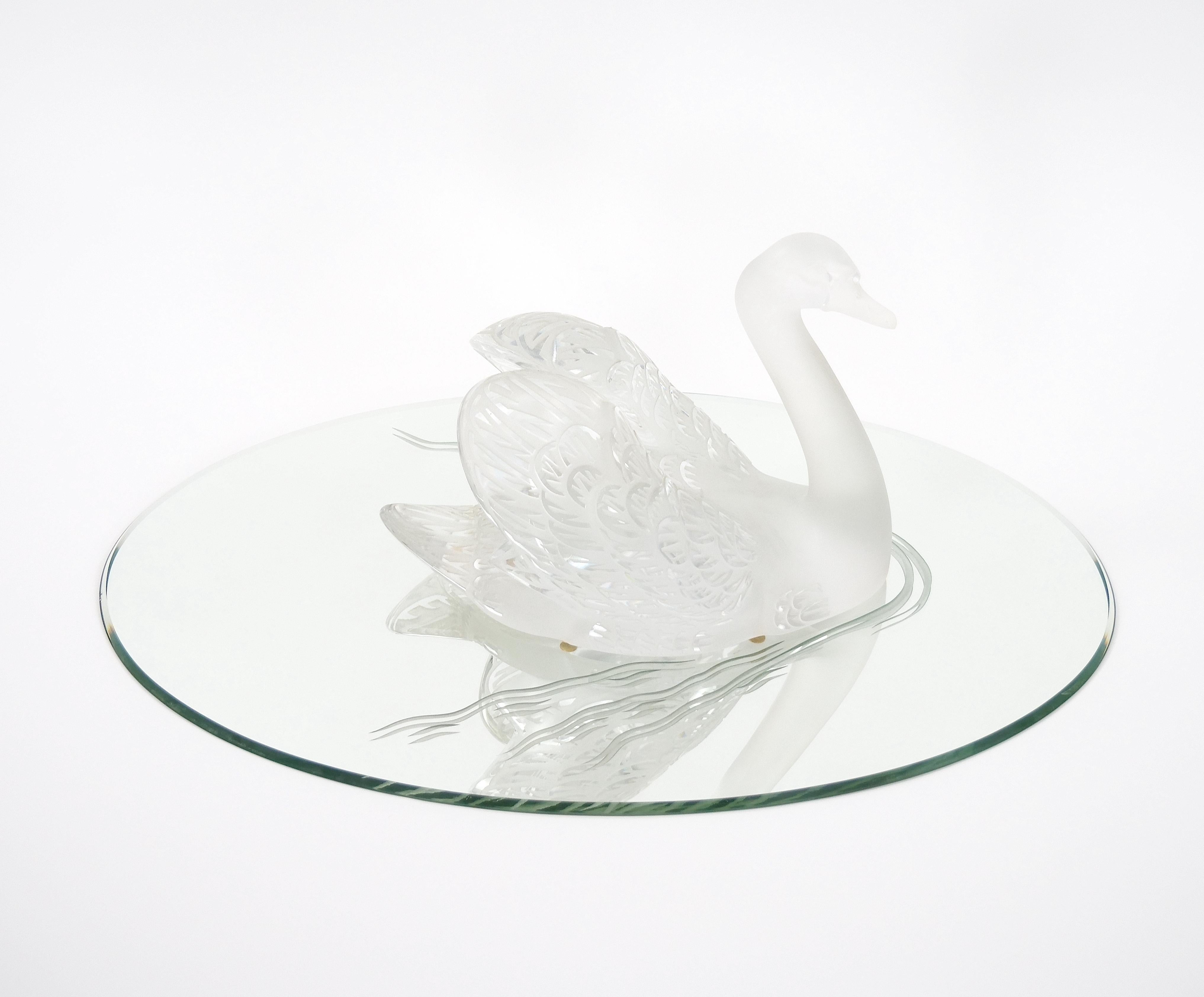 Élevez votre décor avec cette exquise sculpture de cygne givré en cristal de Lalique, élégamment posée avec la tête gracieusement baissée, reposant sur une base ovale ajustée en miroir. Cette sculpture est un véritable chef-d'œuvre d'art et
