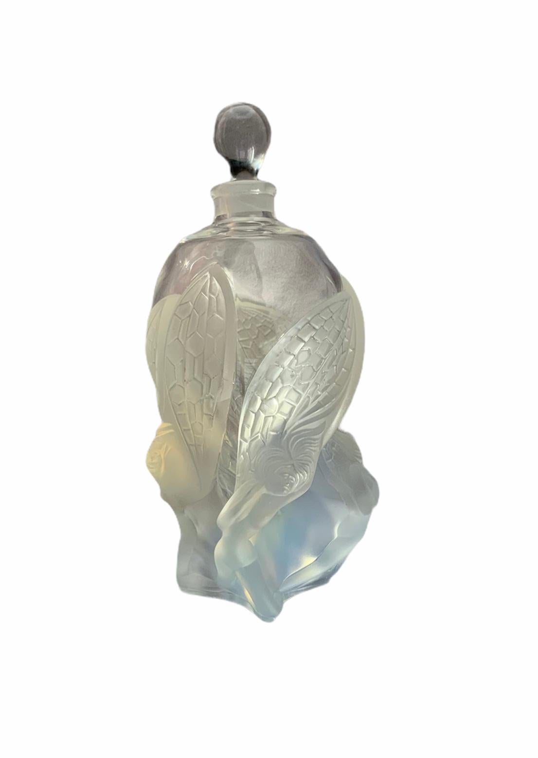 This is a rare Lalique crystal Les Elfes perfume Factice bottle. It depicts an urn shaped clear bottled adorned at the bottom with some embraced opalescent large winged fairies made of frosted glass. The stopper is shaped as an up side down tear