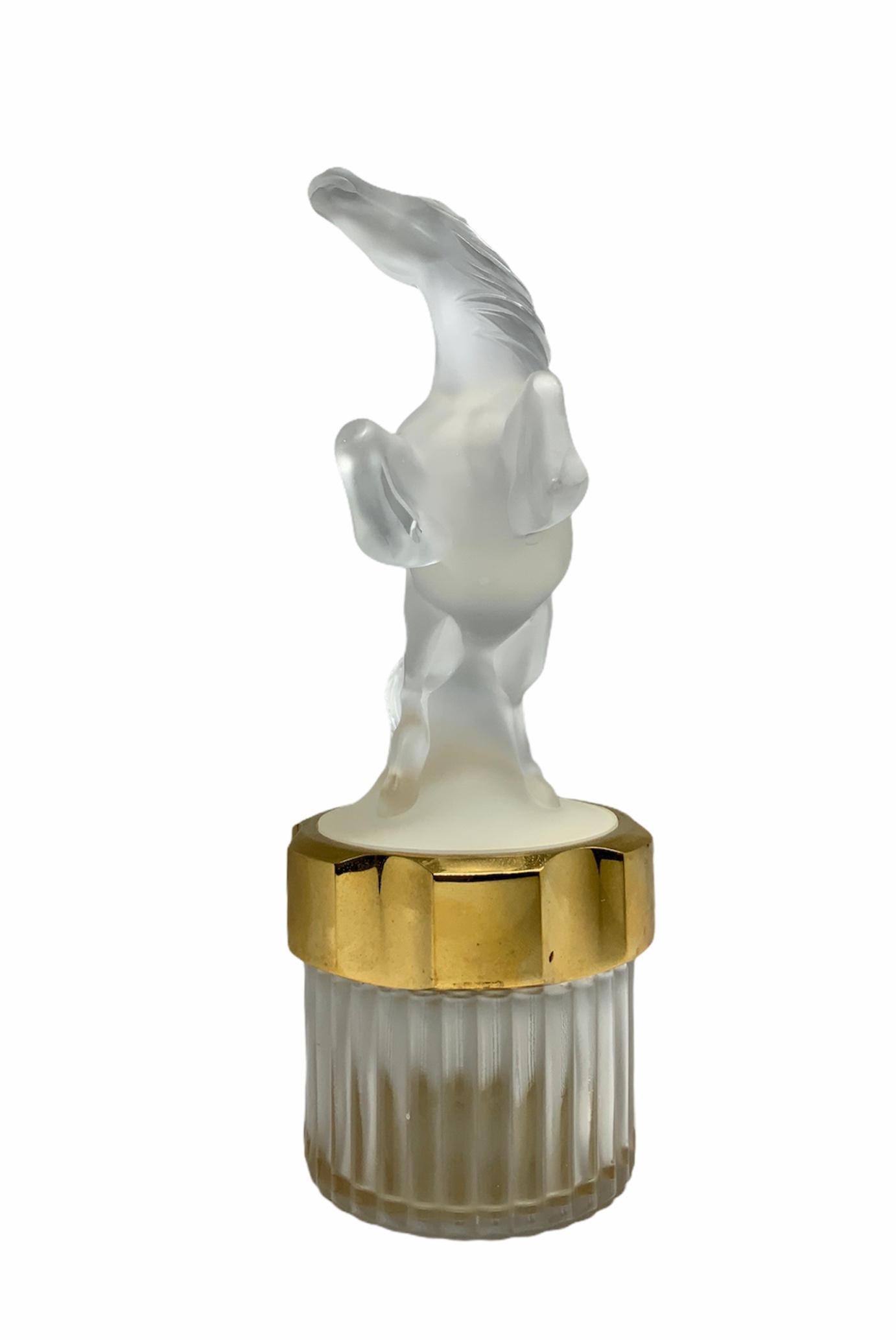 This is a Lalique Crystal Flacon Collection “Mascotte Equus” men perfume bottle. It features a frosted crystal horse standing on his hind legs over a round crystal base surrounded by a gold tone plastic round lid. The clear crystal bottle is ribbed