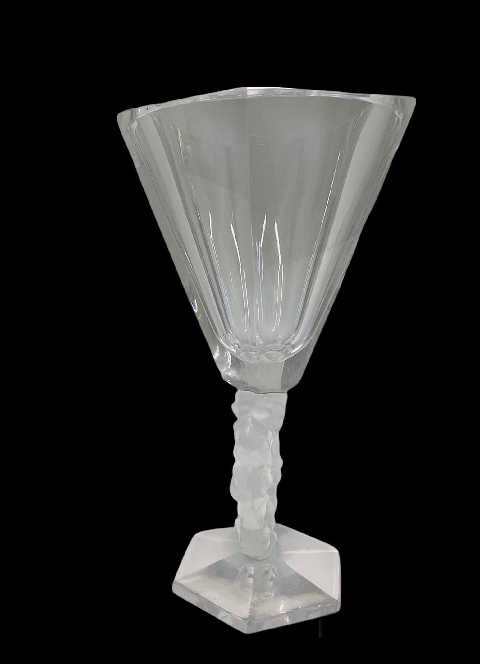 This is a Lalique Crystal Mesange flower vase. It depicts a vase with an hexagonal base followed by a stem shaped as a wreath. The wreath is made of periwinkles flowers decorated in the center by two chickadees birds that appear to be talking and