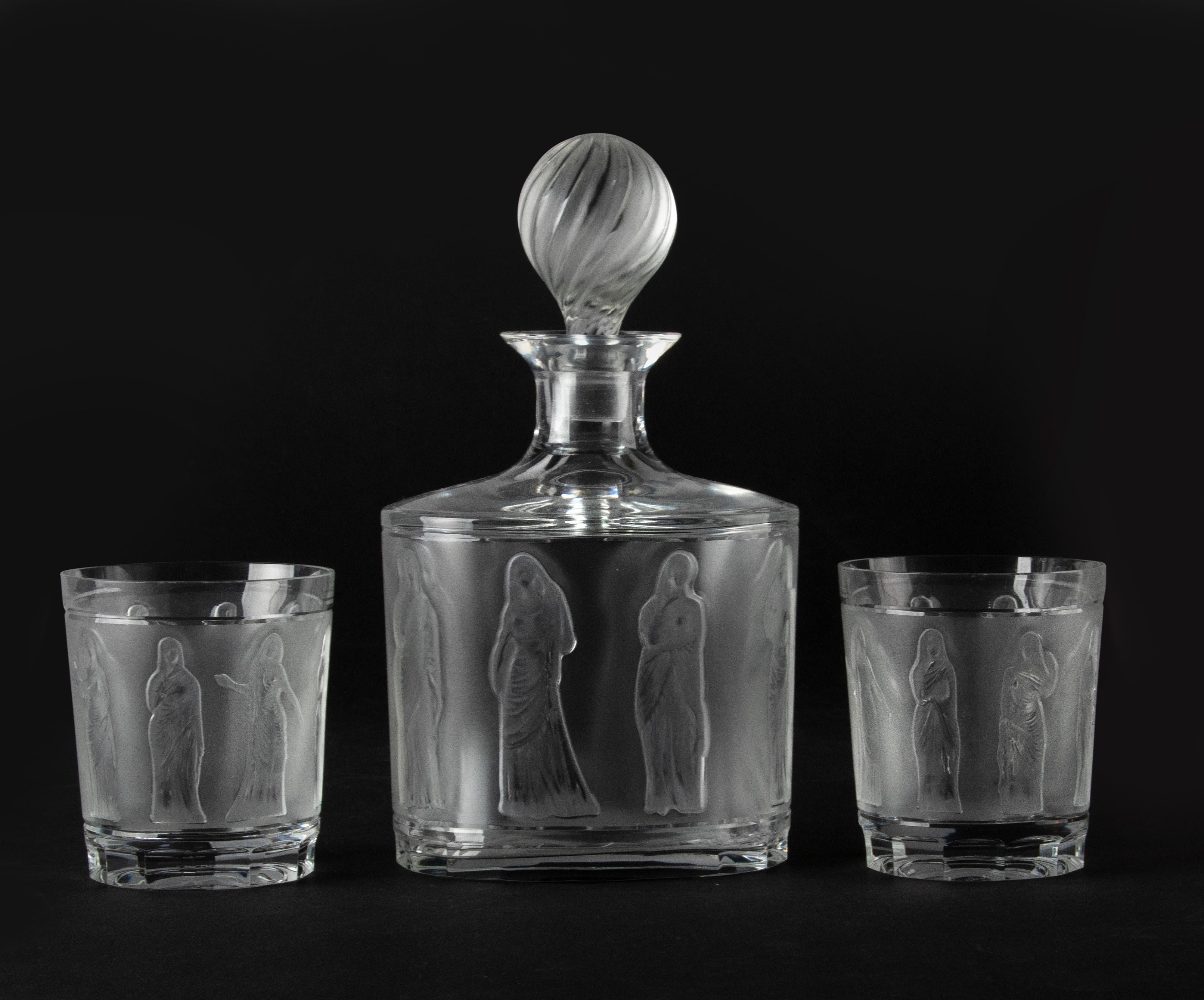 Beautiful crystal decanter from the French brand Lalique with two matching whiskey glasses. The crystal is decorated with classic female figures, the outside of the crystal is satin. The name of this model is 'Femmes Antiques'. All parts are signed