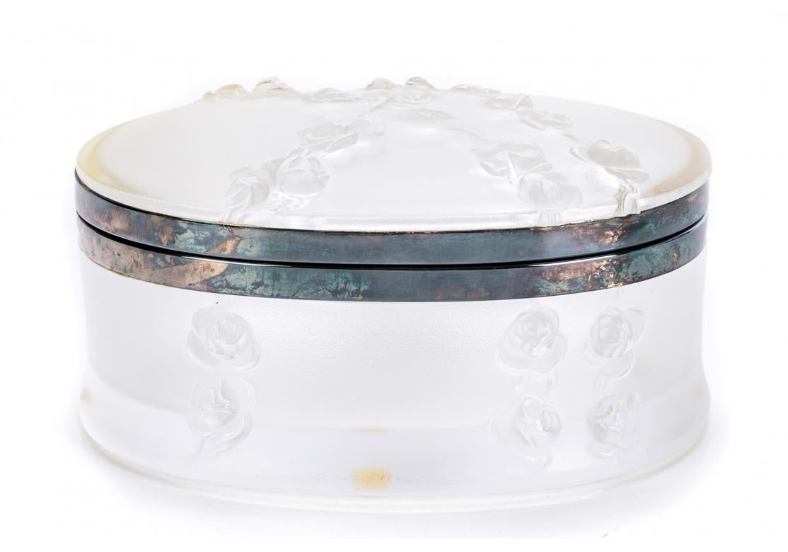 Lalique France Coppelia pattern oval lidded box with metal mounts and hinge, moulded in relief with chains of roses tumbling down the sides. The lid slightly domed, marked on verso and retaining the acrylic sticker.
Dimensions: 7