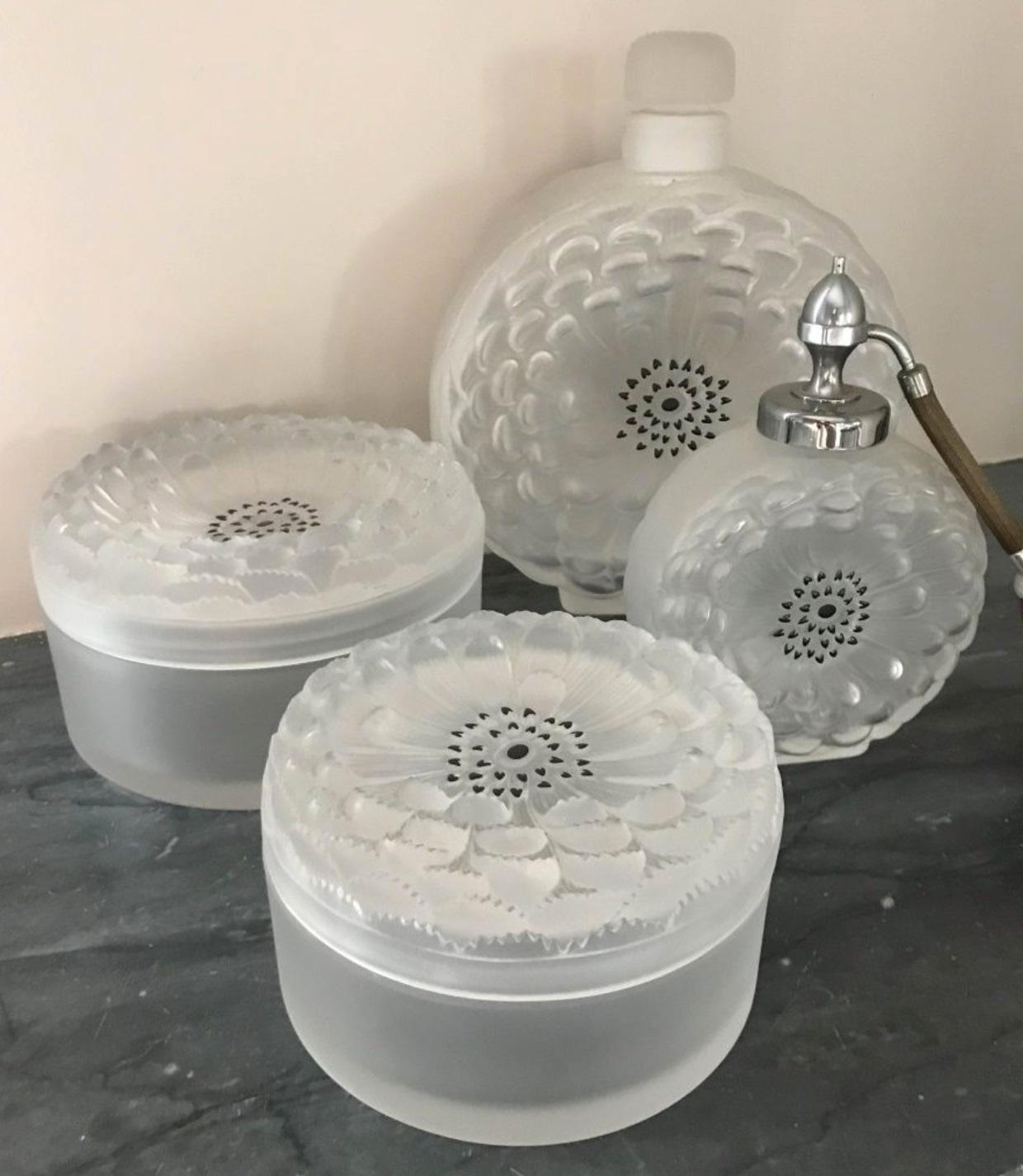 Lalique France, Dahlia.

Toiletries set consisting of two bottles (one covered) and two covered boxes in satin molded pressed glass decorated with Dahlia petals.
1 bottle
1 spray and 2 powder boxes
Signed.
Measure: Height 8.27 in (the biggest
