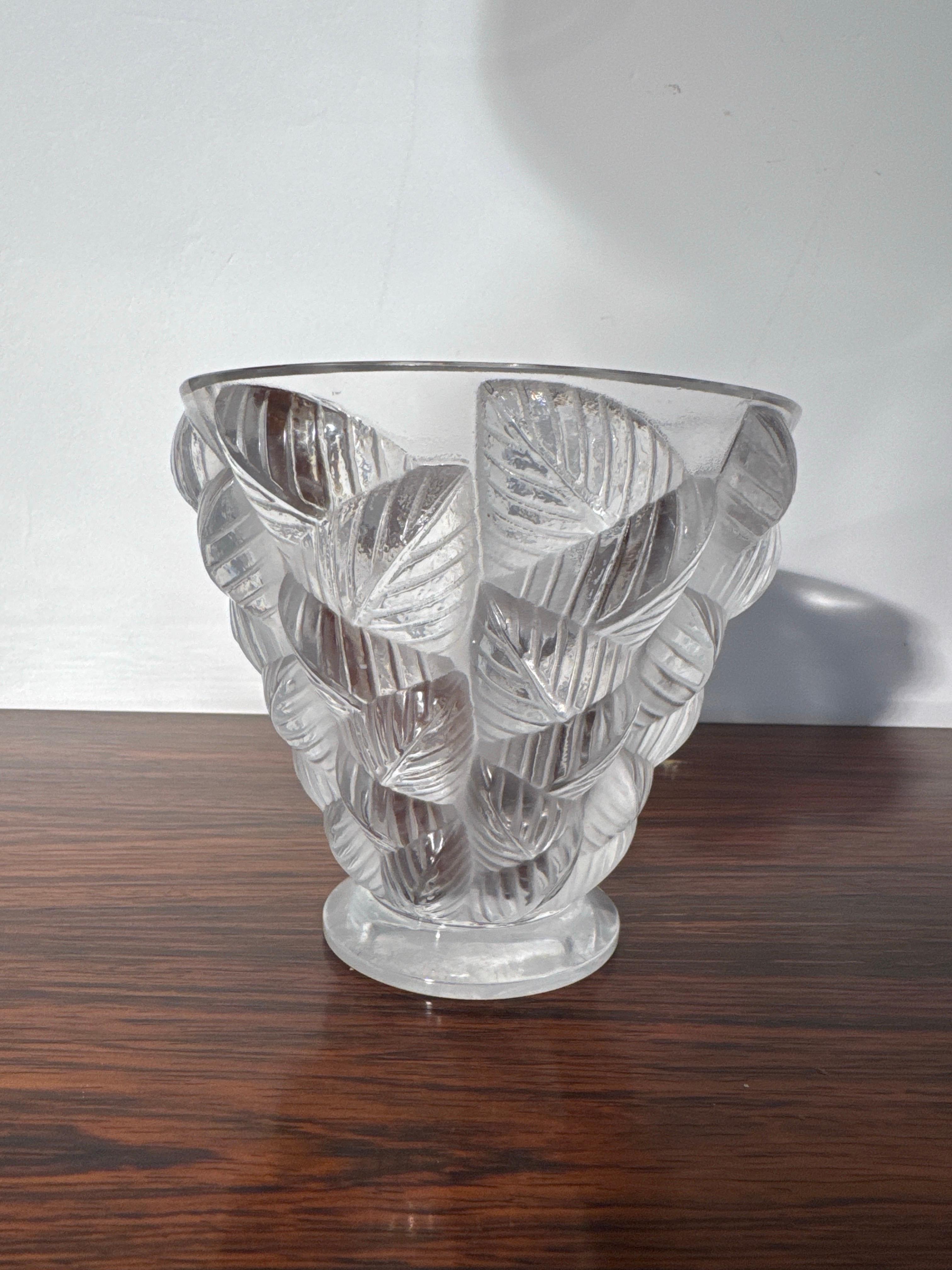 
Jarrón decorativo de Arte Natural firmado 'Lalique France' decorado con hojas de la colección 'Moissac' Francia, años 30. 
El jarrón tiene forma cilíndrica con un borde más ancho, ahusado en la parte inferior, diseñado para evocar la grandeza y