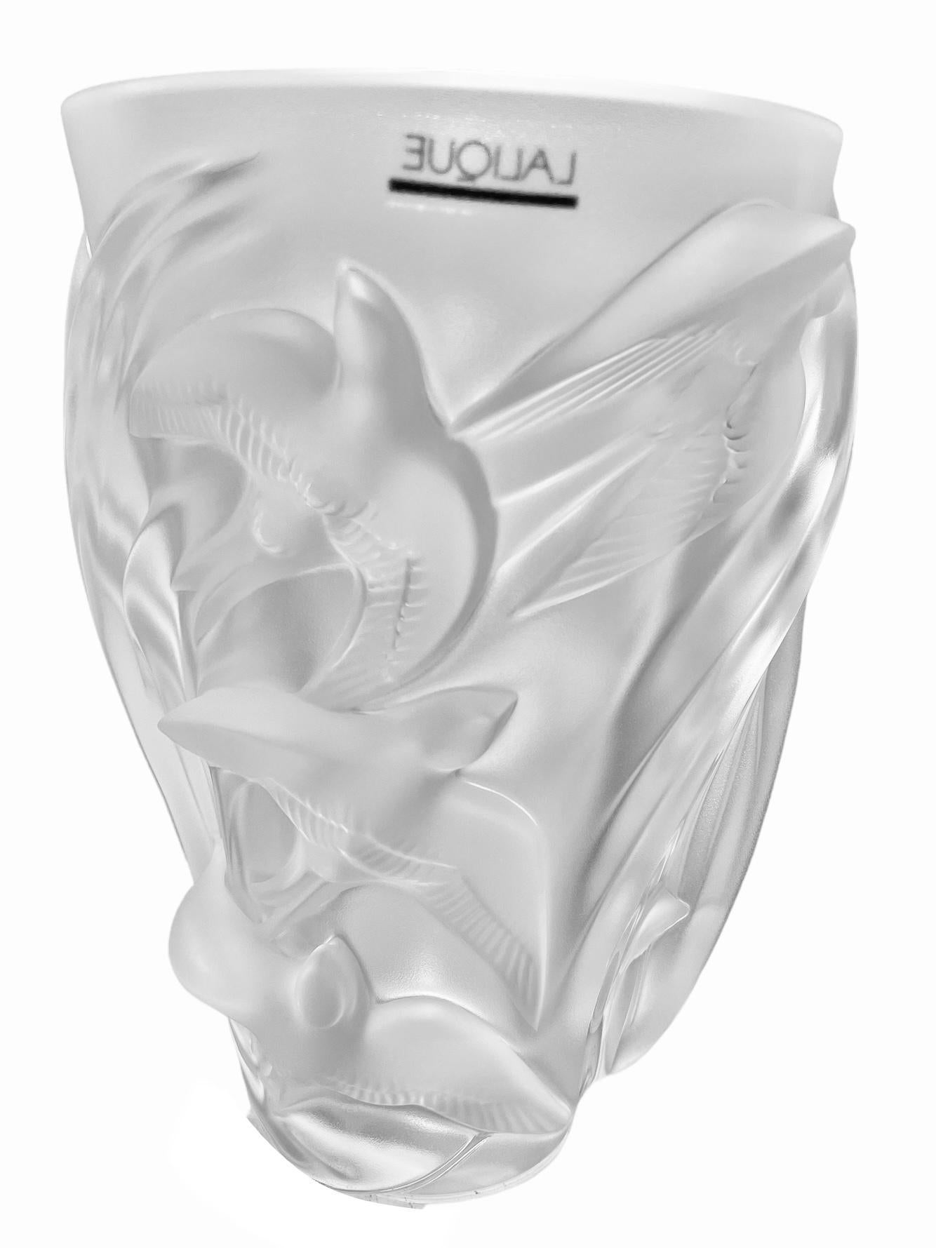 This is an upside down bell shaped, tall & wide flower crystal vase. It is adorned by the relief of several frosted Martinets Sparrow birds that are flying all around. Under the base is marked Lalique, an encircle R, France and in the upper border