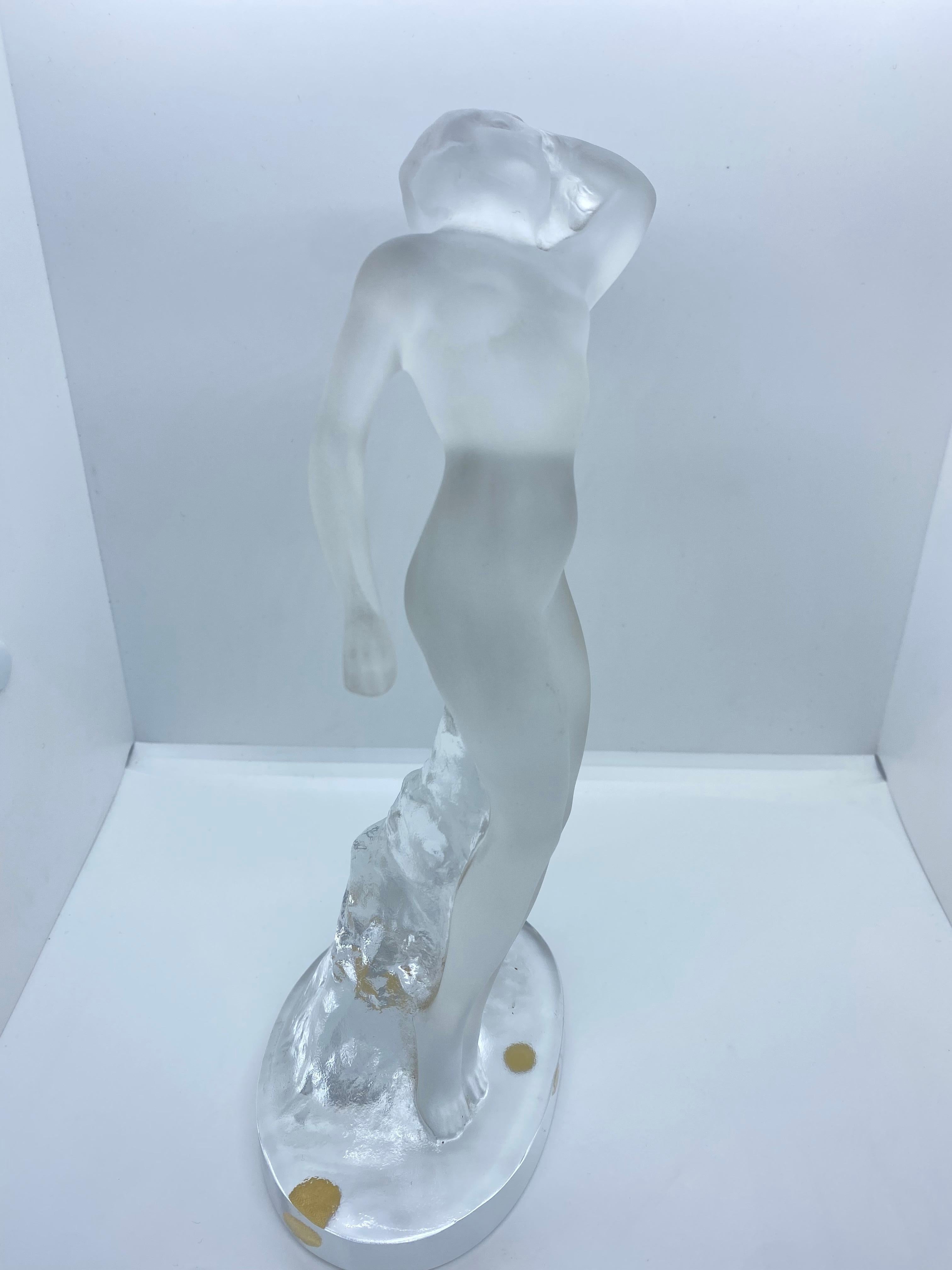 Eine schöne Kristallskulptur einer nackten Frau in erotischer Pose, stilvoll gestaltet. Die Skulptur zeigt eine nackte, mattierte Tänzerin, die mit einem Arm nach oben und einem Arm nach unten auf einem klaren, ovalen Sockel steht. Auf dem Sockel in