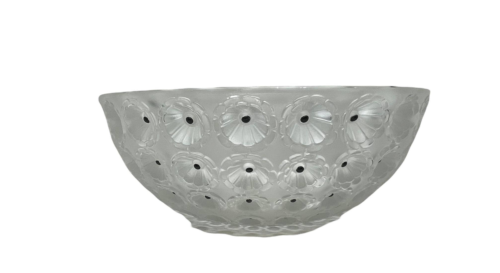 This is a Lalique Nemours crystal bowl. It depicts a frosted clear bowl adorned with multiples rows of flowers with enameled black center dots around it. Below the base, it is found Lalique, France hallmark.