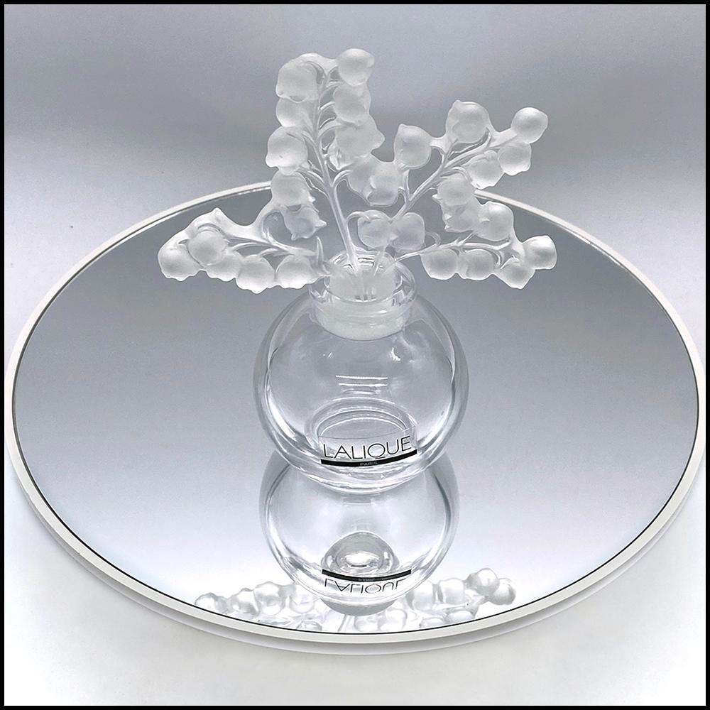 Es handelt sich um einen Parfümflakon aus Kristall mit dem Label Lalique Paris und der Gravur Lalique France und einem Stopfen. Die klare Kristallkugel ist mit einem Maiglöckchen-Stopfen aus mattiertem Glas versehen. Stellen Sie ihn auf eine