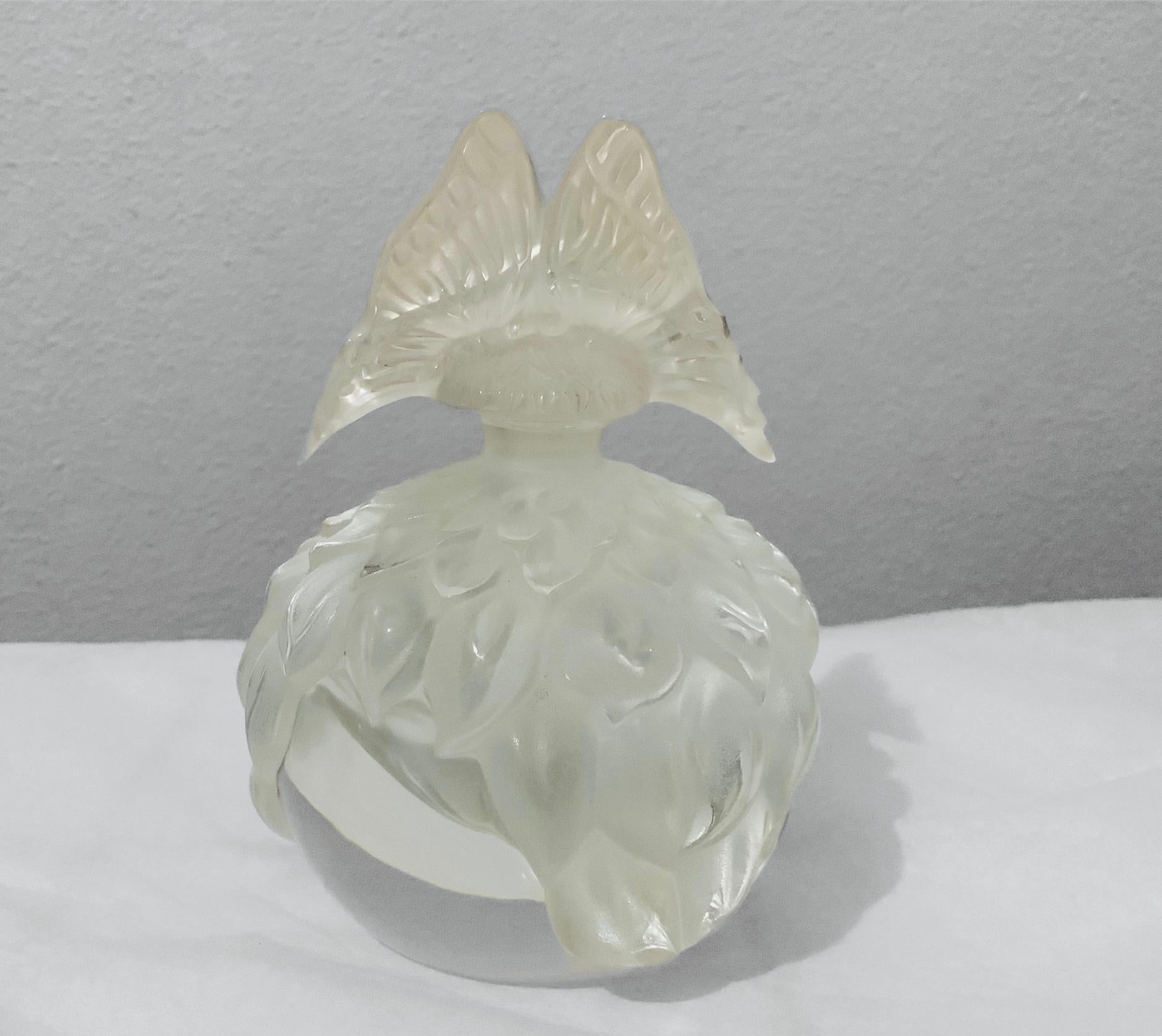 This is a limited edition Pristine Butterfly perfume bottle. It is a round clear bottle depicting some relief of frosted leaves around it. The stopper is shaped as a butterfly. Below the bottle there is a plastic sticker and also is hallmarked