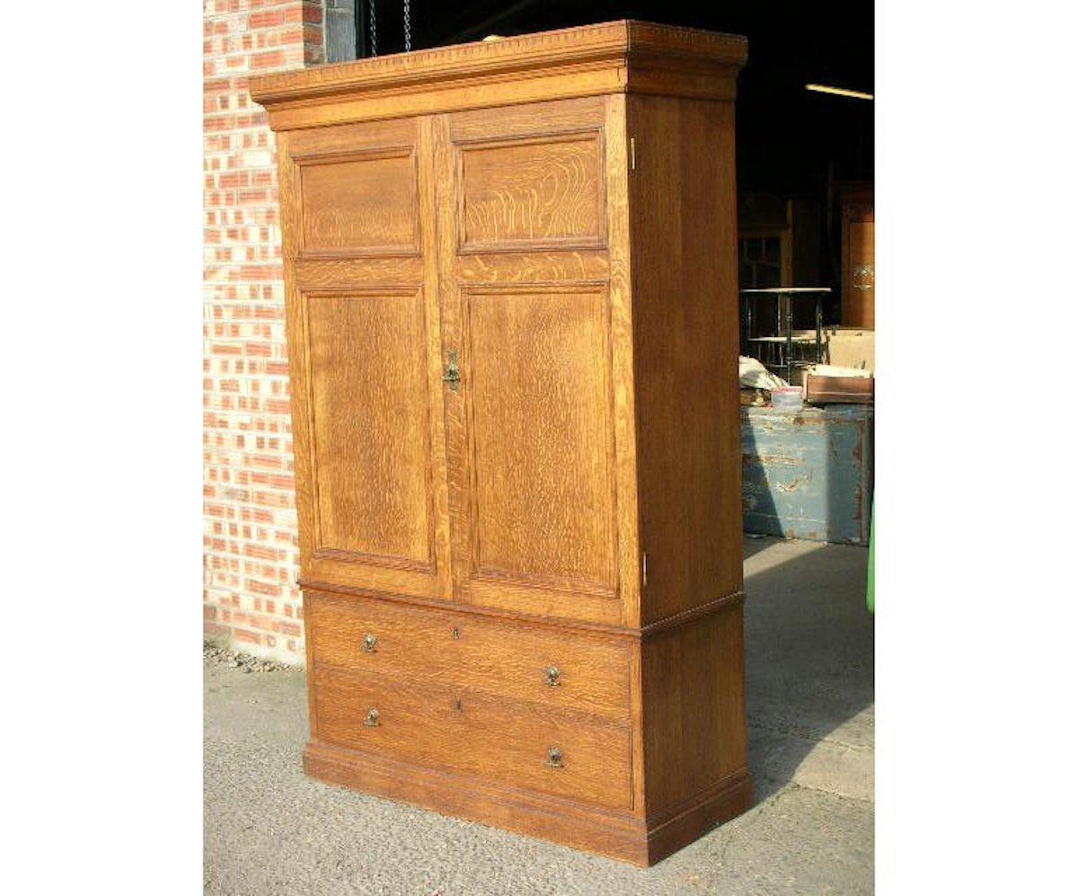 Lamb of Manchester. An Aesthetic Movement Arts & Crafts style compactum armoire wardrobe with castellated cornice and twin fielded panel doors opening to reveal hanging space to the left and four open slides and two smaller drawers to the right with