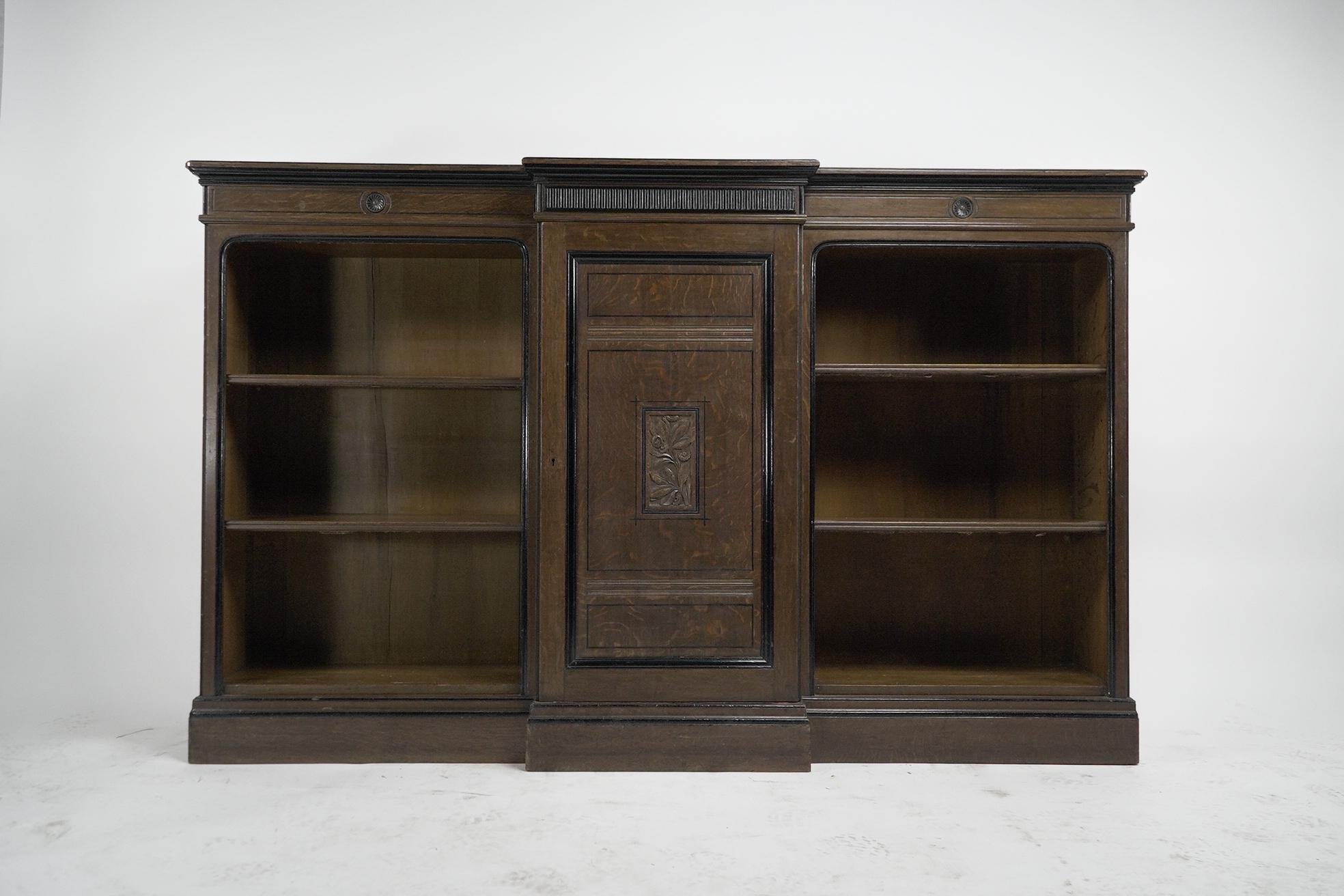 Lambs of Manchester, stamped to the brass door lock. A fine Aesthetic Movement breakfront bookcase made from quarter sawn oak with a raised back to the top and fluted decoration below the top display area, flanked by carved florets with further