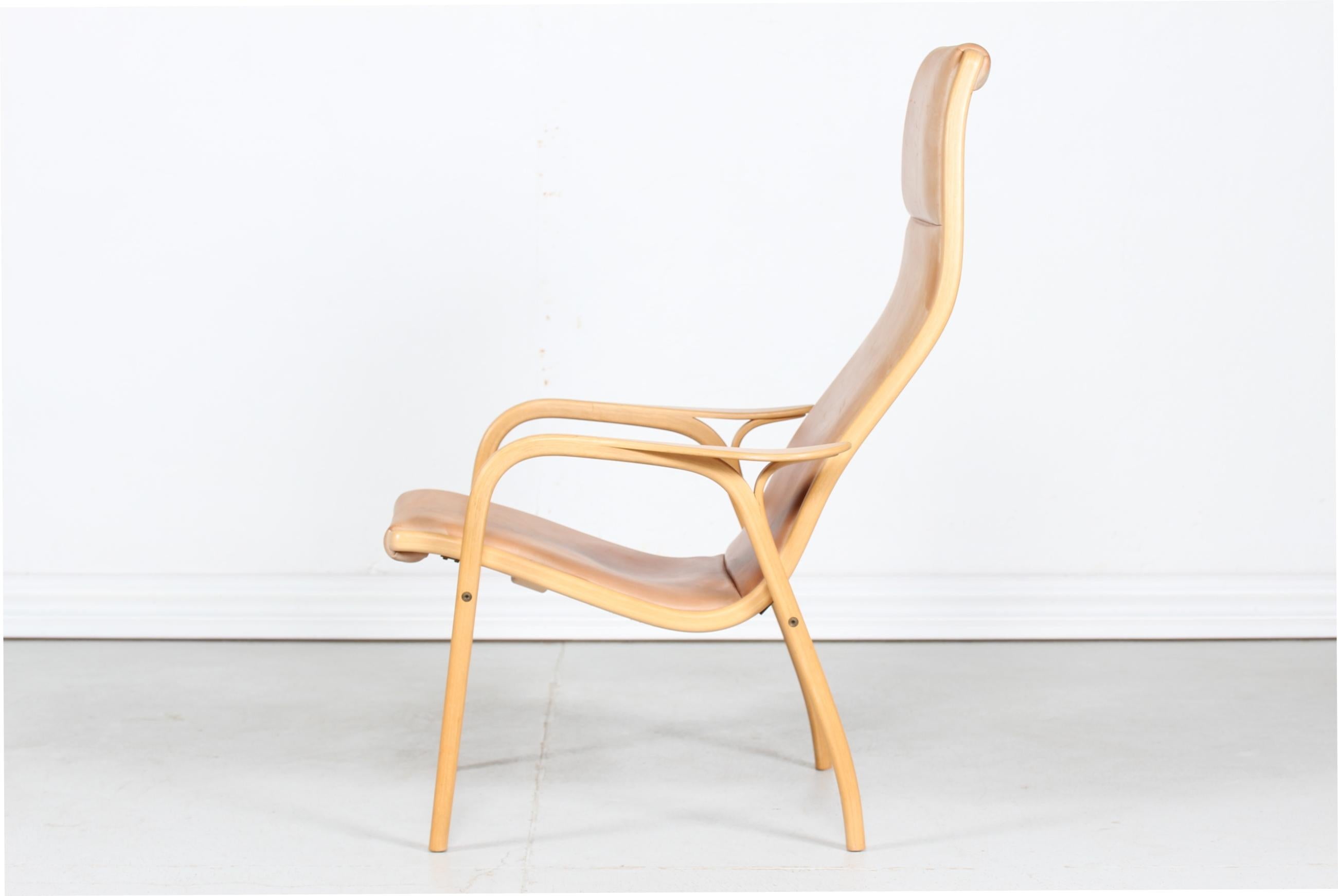 Lamino lounge chair and stool with frame of steam bend plywood of beech and smooth cognac colored leather seats.
The set is designed by Yngve Ekström (1913-1988) in 1956 and manufactured by Swedese Möbler in Sweden in the 1980s.

Measurements: