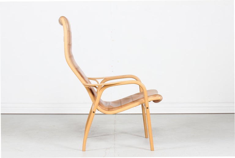 Lamino lounge chair with frame of steam bend plywood of beech and smooth cognac colored leather seats. This particular item is with leather stitching. 
The lounge chair is designed by Yngve Ekström (1913-1988) in 1956 and manufactured by Swedese