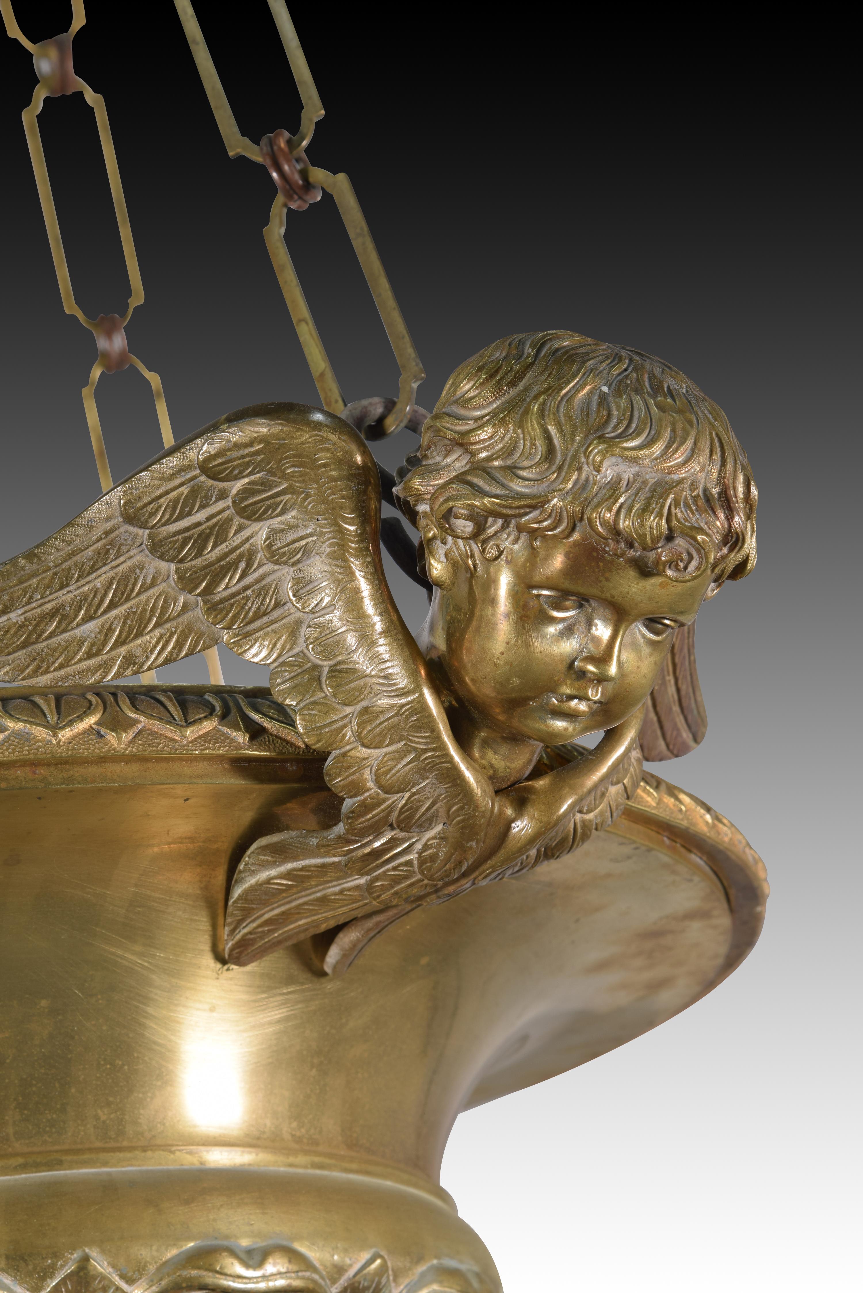 Lamp. Bronze. XIX century. Lamp with circular glass
decorated with a series of classicist decoration moldings
at the bottom and an oval shape from which a
ring hangs, and another molding at the top joining
three heads of winged angels From the back