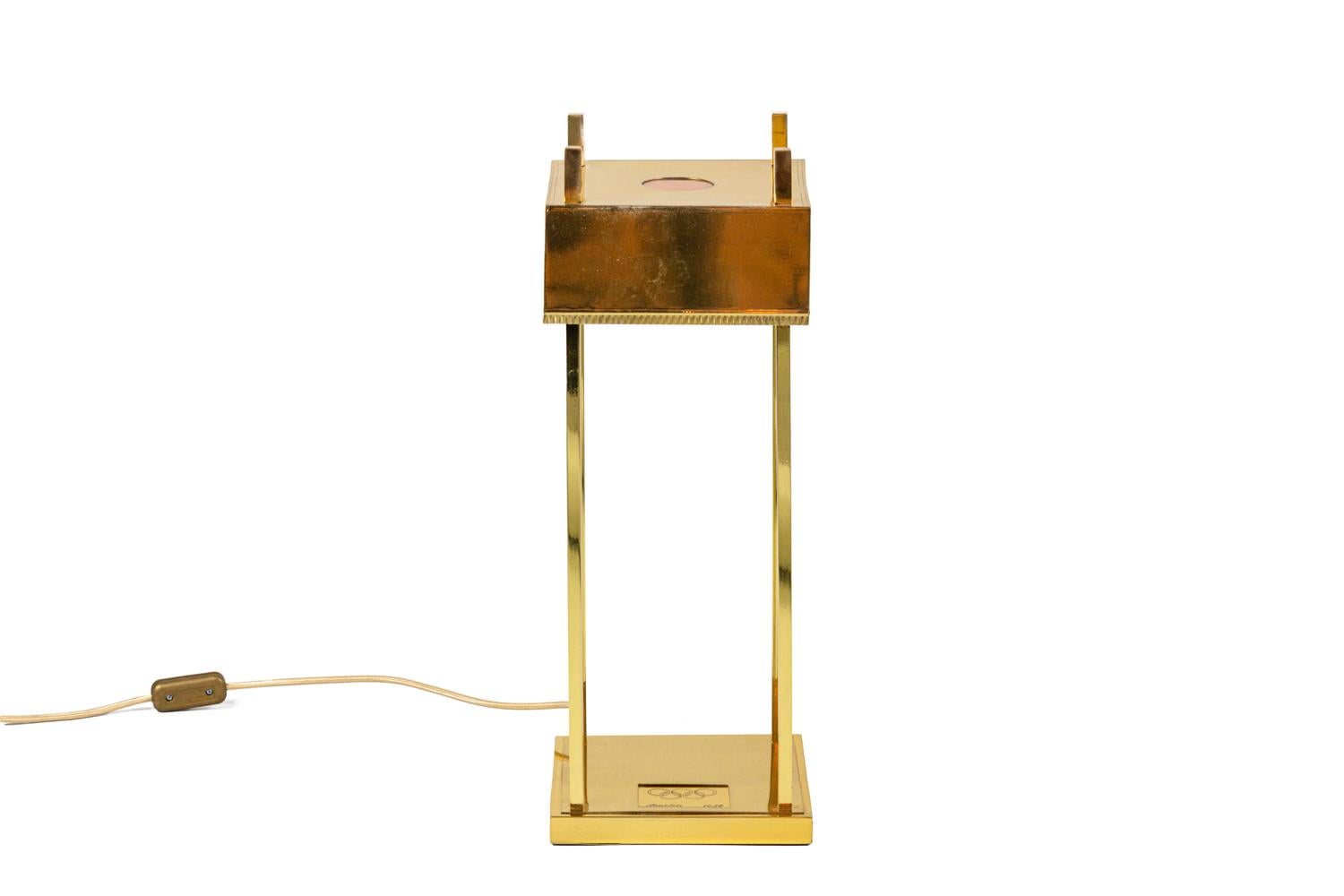 Lamp in gilt brass with a square lampshade adorned with copper rounds and a trygliphs frieze. It stands on four square section sticks fixed on a square base engraved with the Olympic Games logo.

Numbered 1357 and engraved “WerkeAG” on the