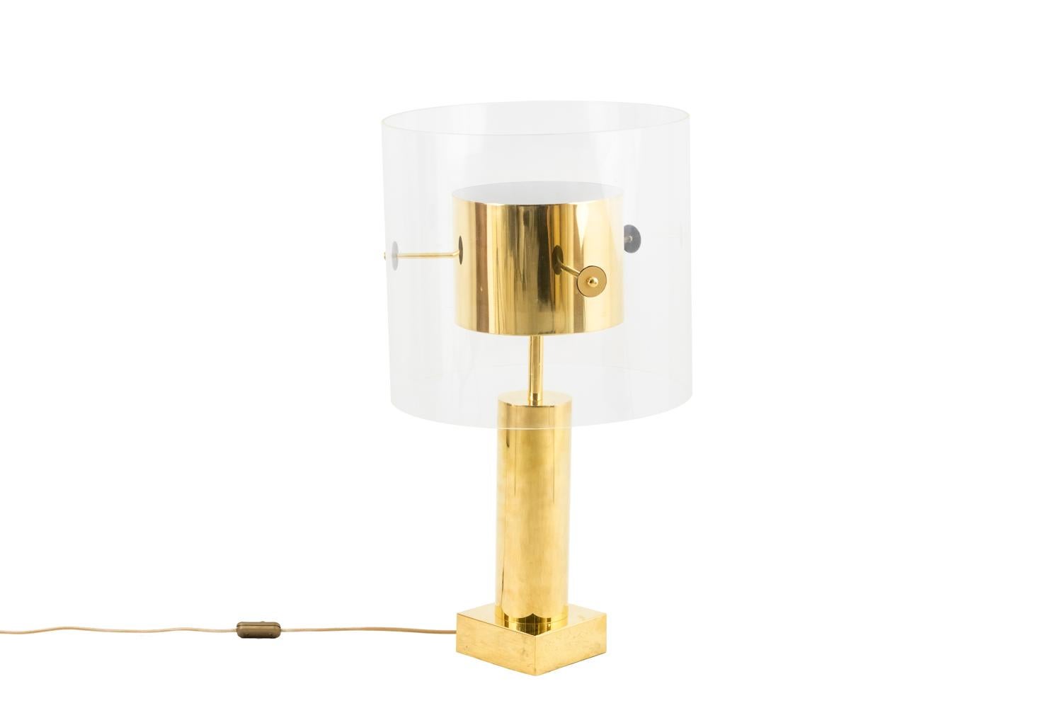 Lamp in gilt brass and Lucite. Shaft in cylindrical column shape standing on a square base. It is topped by a stick and a cylinder on which three sticks are fixed, themselves fixed to the Lucite cylindrical lampshade.

Work realized in the