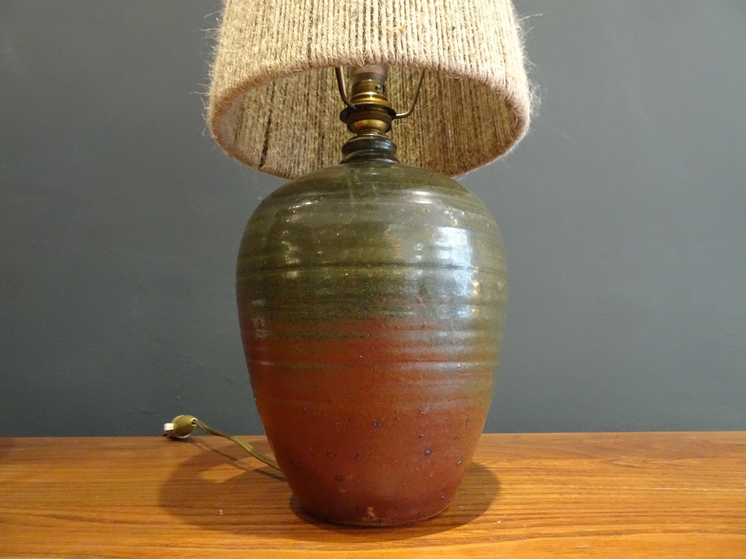 Signed lamp in green and red enameled sandstone and lampshade in light colored cords. 
 
Dimensions: 43cm high, lampshade diameter 15.5cm

Very good condition.