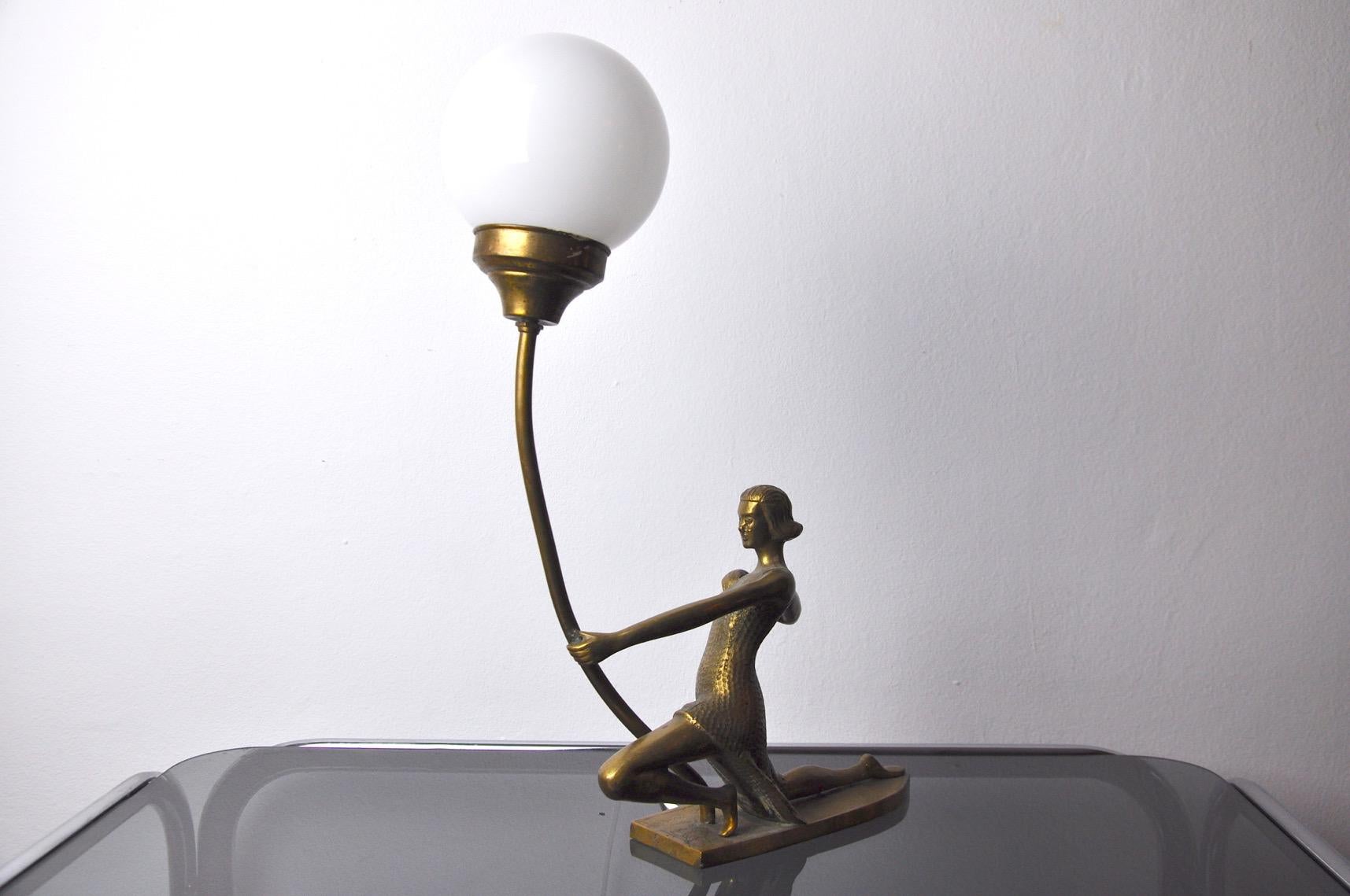 Very beautiful art deco table lamp representing a woman shooting an archery, designed and produced in France in the 1950s. Brass lamp and its opaline globe in perfect condition. This design object will illuminate your interior wonderfully. Lamp