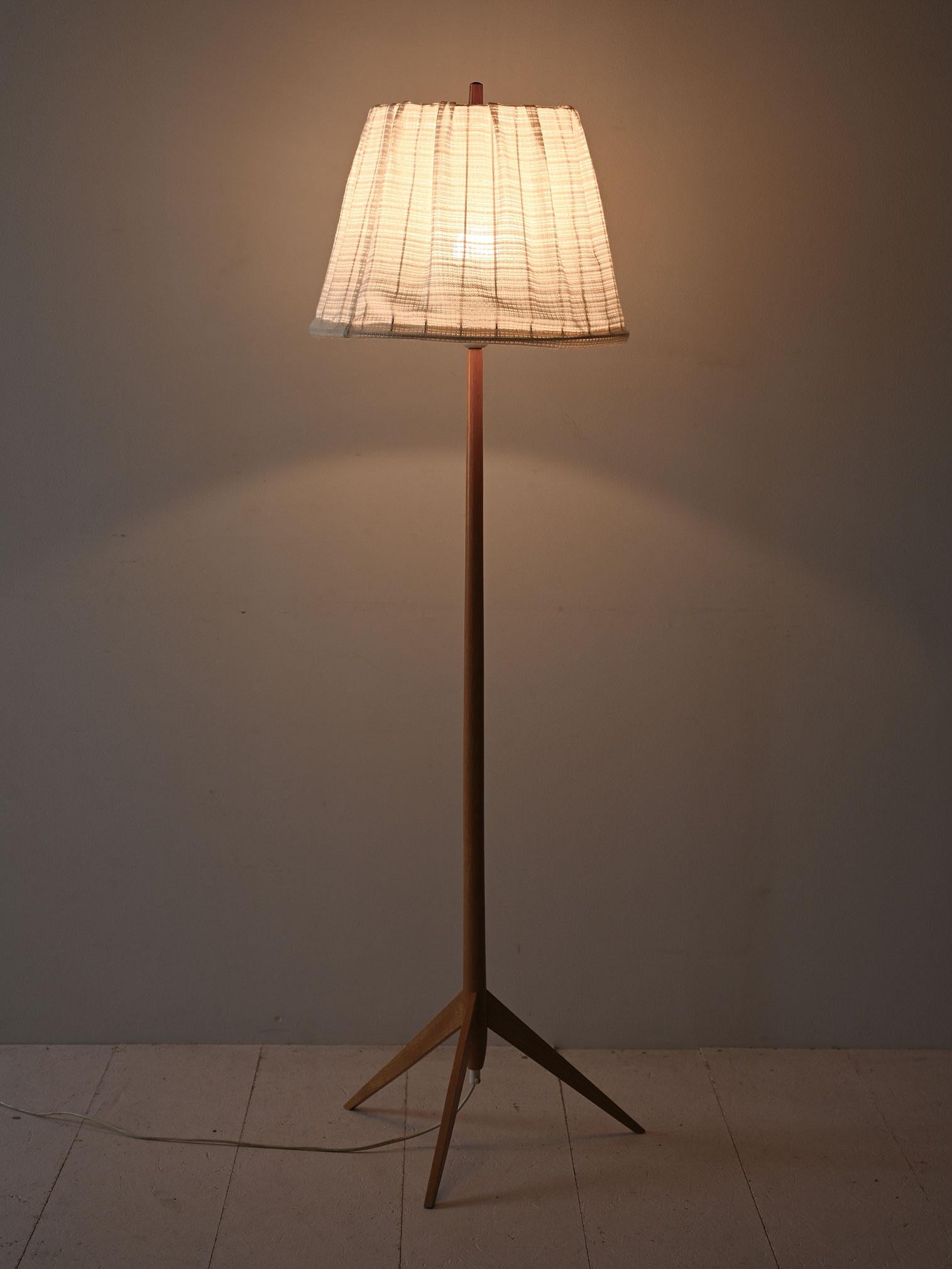 1960s floor lamp with natural wood frame and light fabric shade.

 The natural wood frame features a tapered stem that widens into a tripod base. The light fabric lampshade diffuses a soft, welcoming light. Good conditions. Potrebbe presentare dei