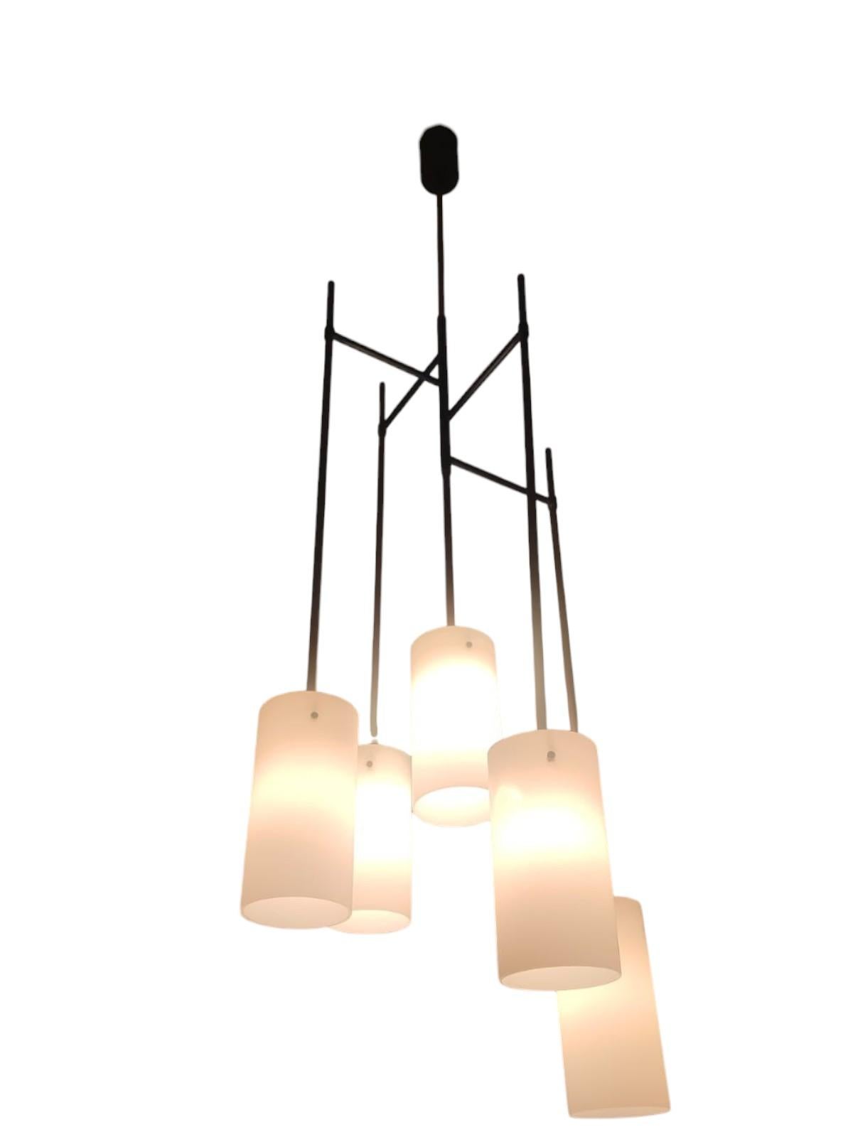 Lampada a sospensione a cinque luci in vetro opalino e metallo, produzione Stilnovo degli anni '60.
Il lampadario, dal design minimal ed elegante, è composto da cinque cilindri in vetro opalino a cascata, disposti in varie altezze, sostenuti da aste