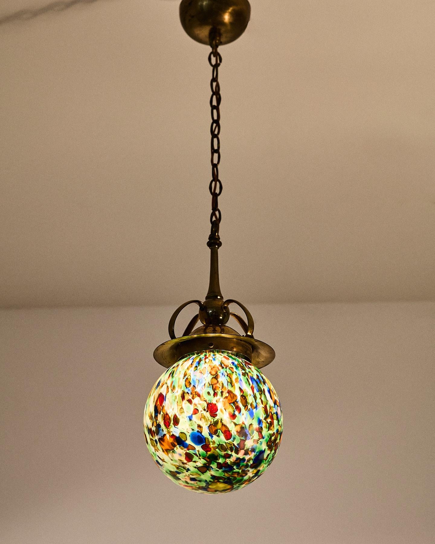 Lámpara colgante Art Nouveau, fabricada en Italia a principios del siglo XX.
La elegante estructura de latón bruñido, adornada con sinuosos motivos curvilíneos inspirados en el mundo floral, soporta un difusor esférico de cristal de Murano