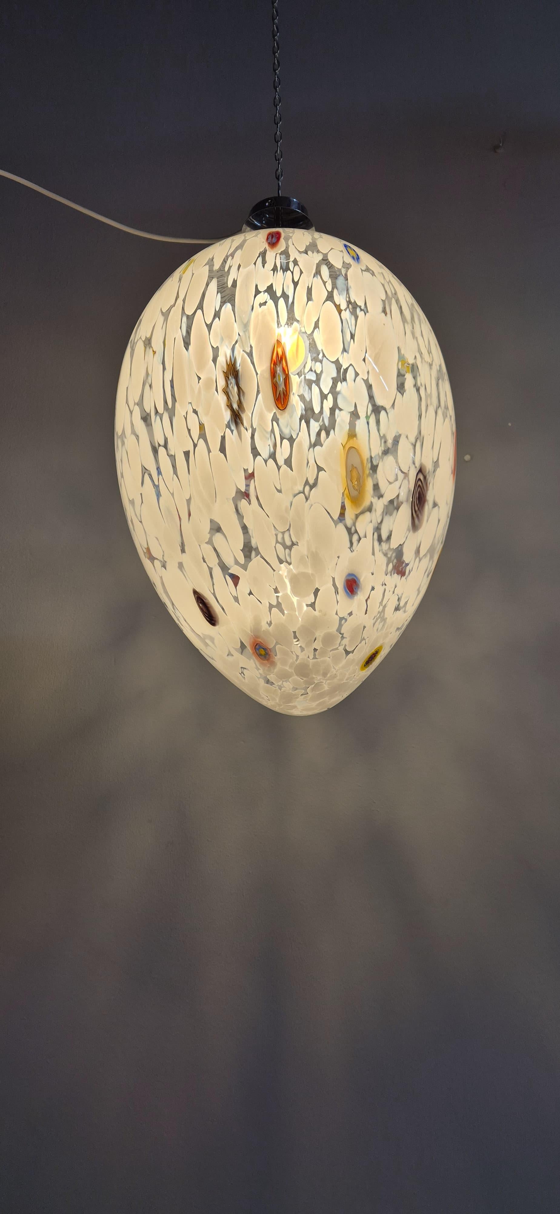 Bellissima e particolare lampadario Egg in vetro di Murano. Base in metallo, il lampadario ha una forma di uovo, è in vetro di Murano trasparente con decori bianchi e Murrine colorate.