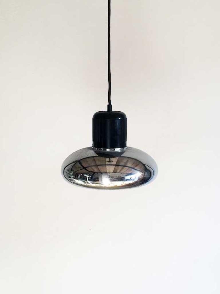 This pendant lamp was designed by Gae Aulenti and manufactured by Stilnovo, consiting of a cast body of black makrolon and of a metal chromed reflector with enameled white inside.  Natural sign and scuffs due to age and use.