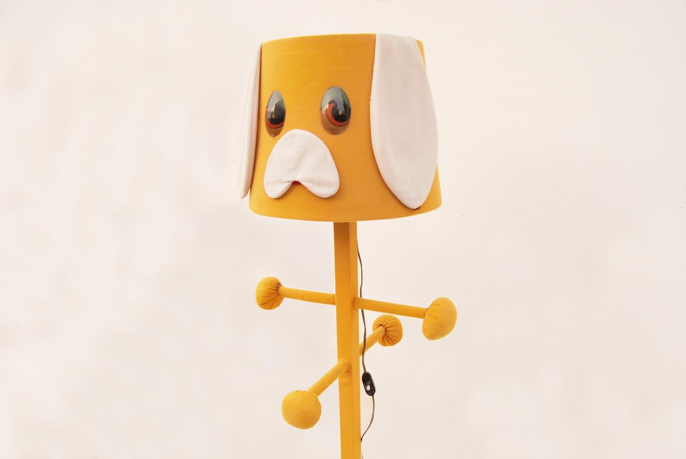 Lampada appendiabiti vintage per camera da ragazzi risalente agli anni '70.
Questo simpatico oggetto è stato realizzato con struttura in legno, rivestita di morbido tessuto, così come il paralume raffigurante il simpatico muso di un