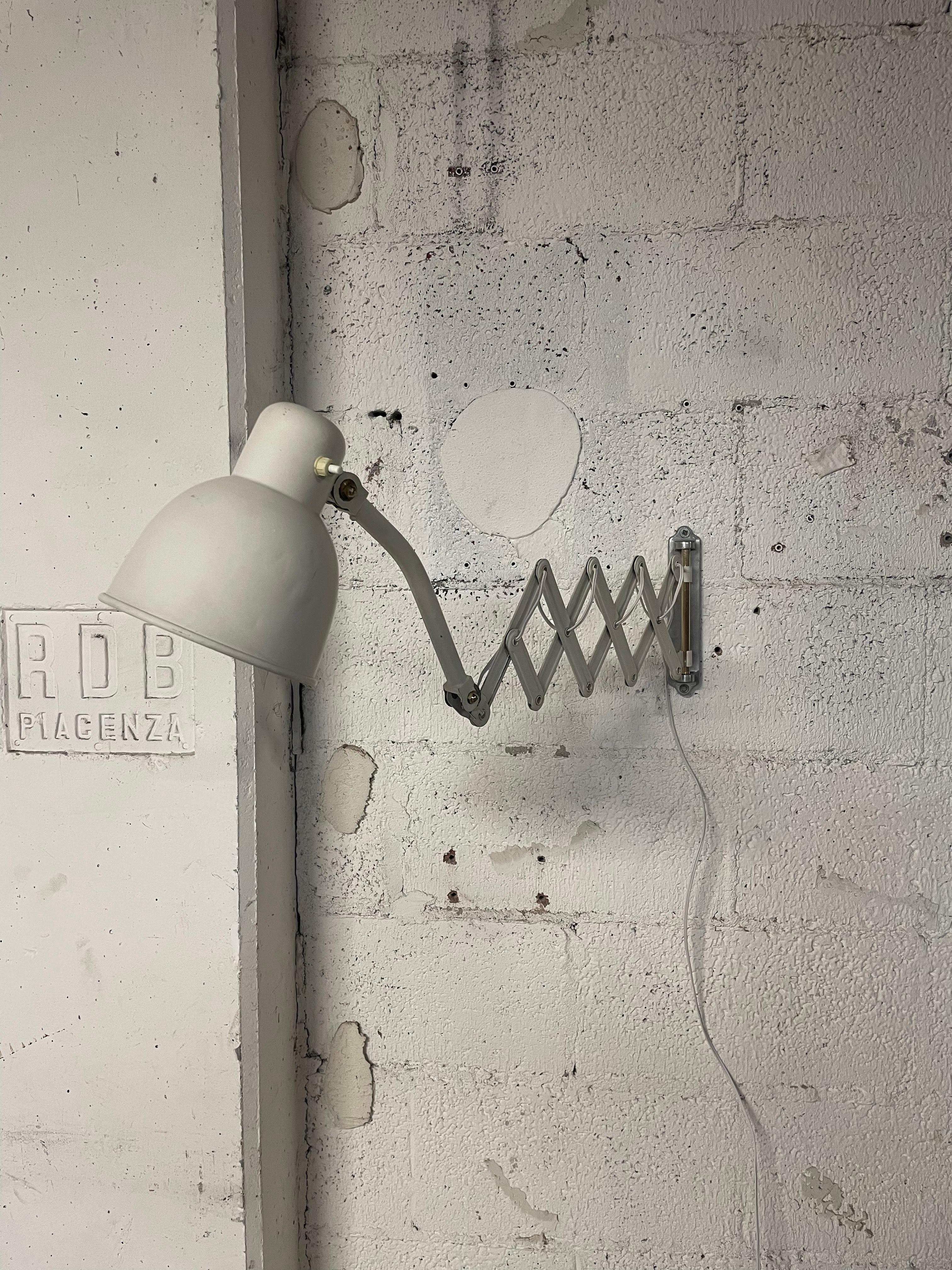 1950s pantograph wall lamp made of white lacquered metal with brass and aluminum details.

Arm extension ranges from a minimum of 40 cm. to a maximum of 90 cm.

Plugs into the socket.