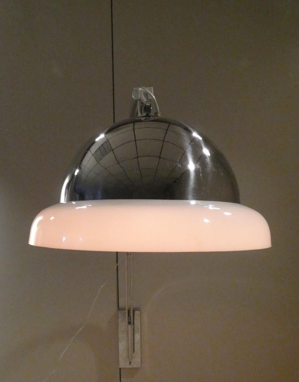 Un connubbio fra un'applique ed un'illuminazione ad arco, così Goffredo Reggiani disegna questa bellissima lampada da parete, rispettando le proporzioni di una lampada da terra a luce diretta, con stelo telescopico adattandola sapientemente al