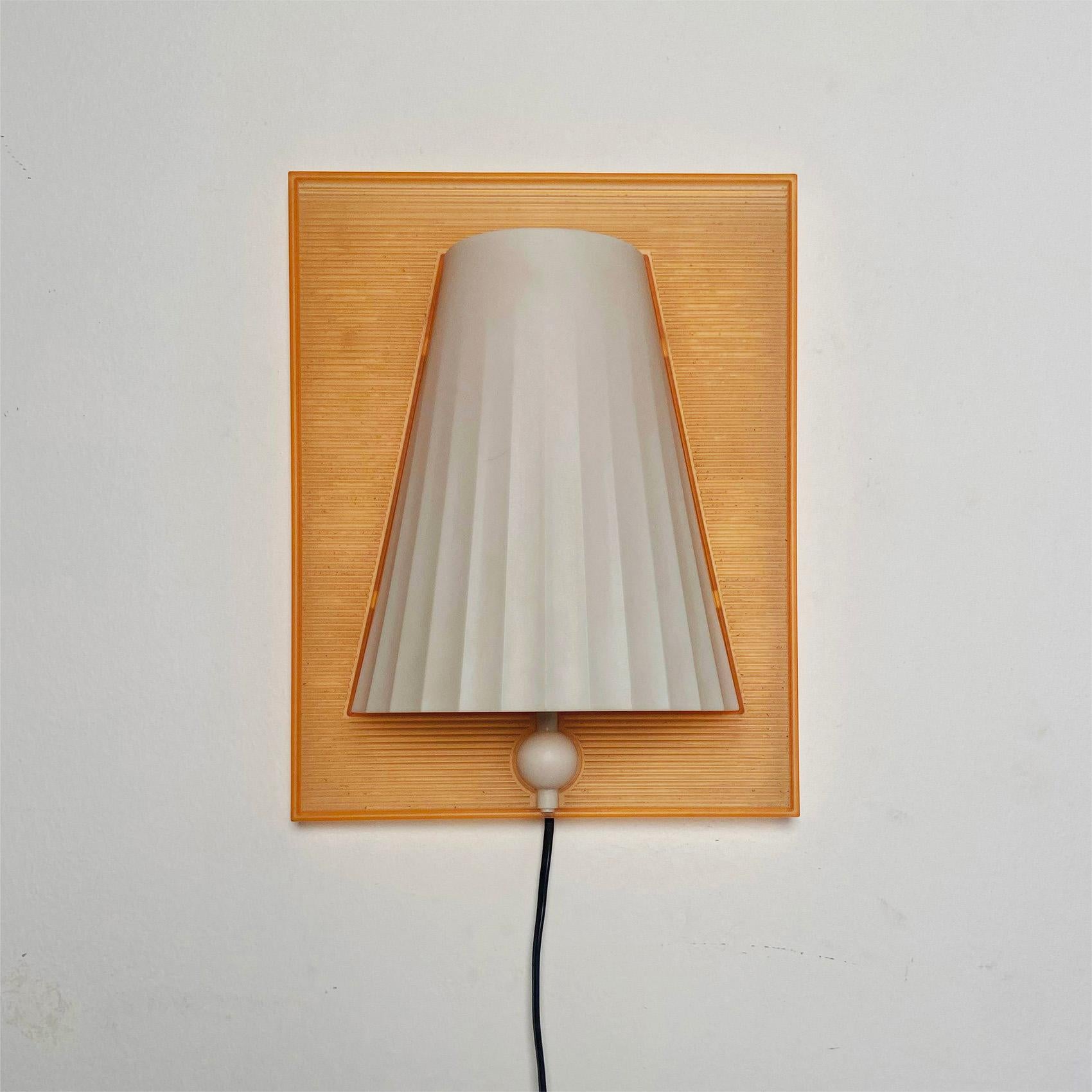 Lampada da parete Walla Walla disegnata da Philippe Starck e prodotta da Flos nel 1994. Pensata per un ambiente che non rinuncia all’eleganza né alla funzionalità, la lampada presenta la particolarità di poter inserire dei fogli colorati