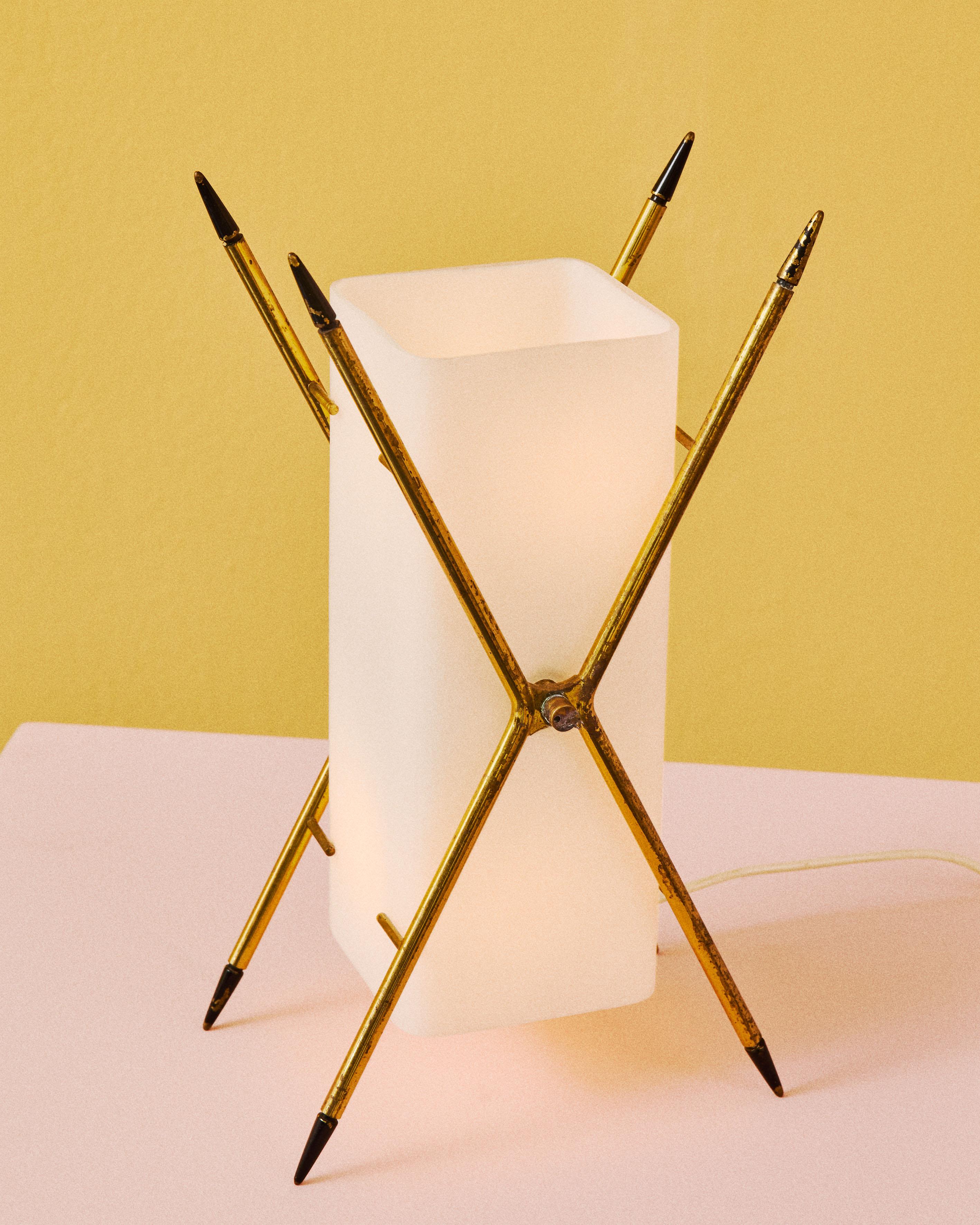 Lampada da tavolo con supporti in ottone lucido verniciato a forma di X e diffusore in vetro opalino bianco, deisgn di Angelo Lelii per Arredoluce, Italia, anno 1957. La forma a X della lampada, pur suggerendo una forma verticale, permette di