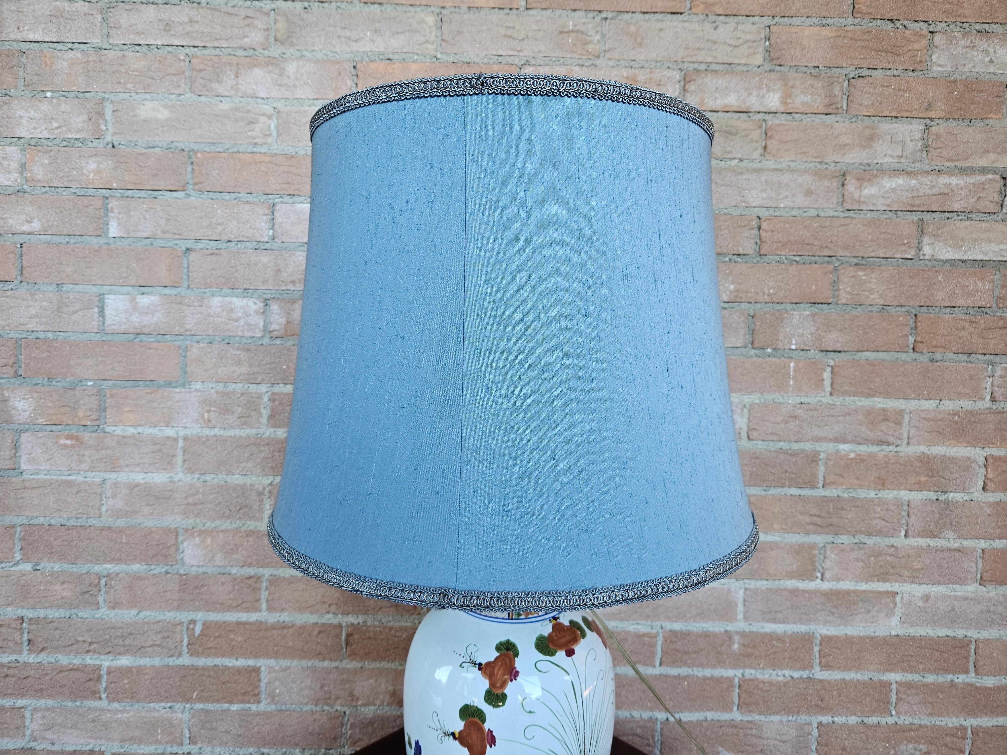 Large ceramic table lamp decorated with floral work and light blue/blue fabric shade.

Bulb not included.
