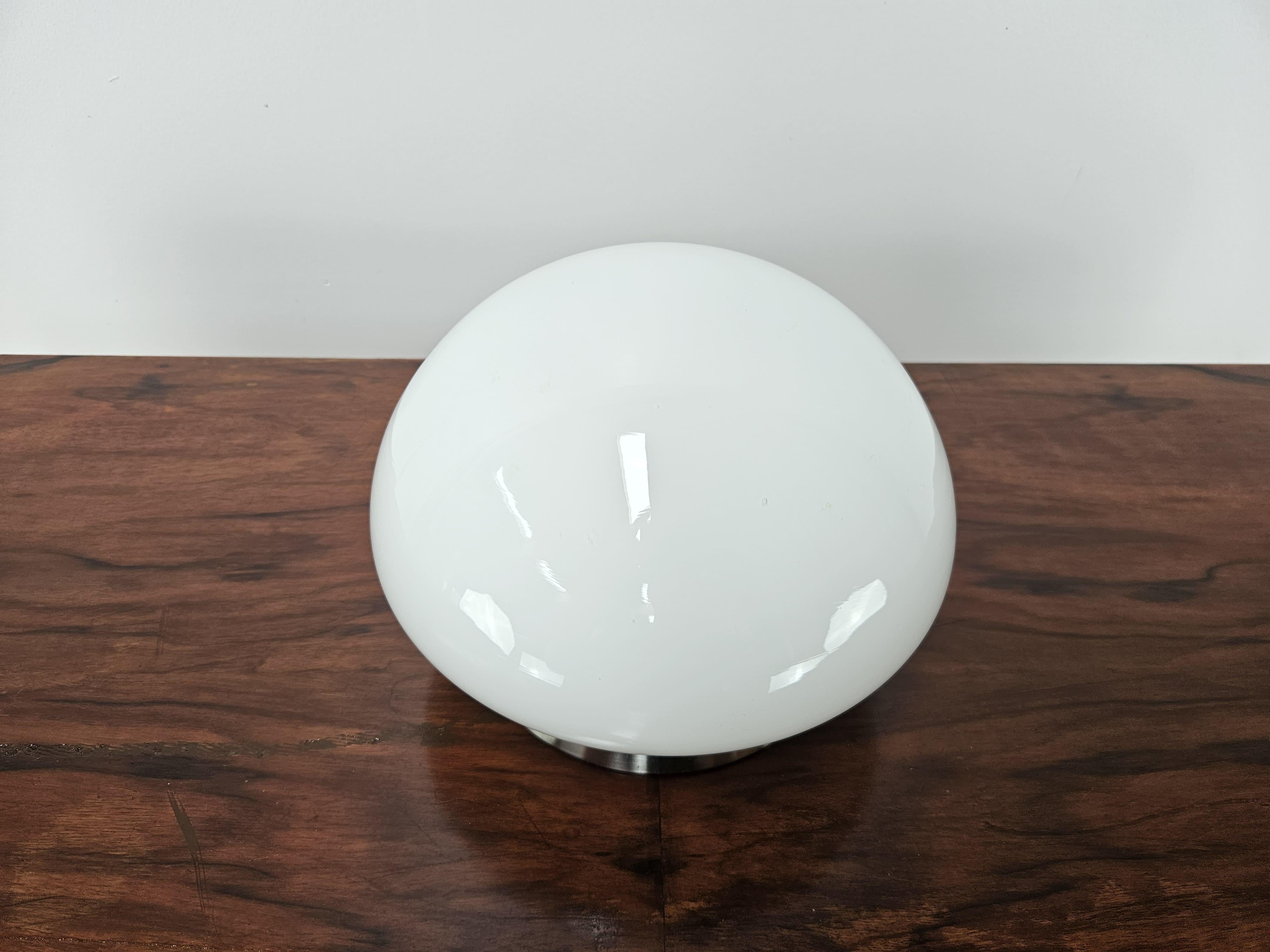 Lampe de table champignon des années 1970 avec base en métal et plafonnier en verre blanc.

Très spécial pour son allumage par contact avec la base métallique.

Signes normaux dus à l'âge et à l'utilisation.