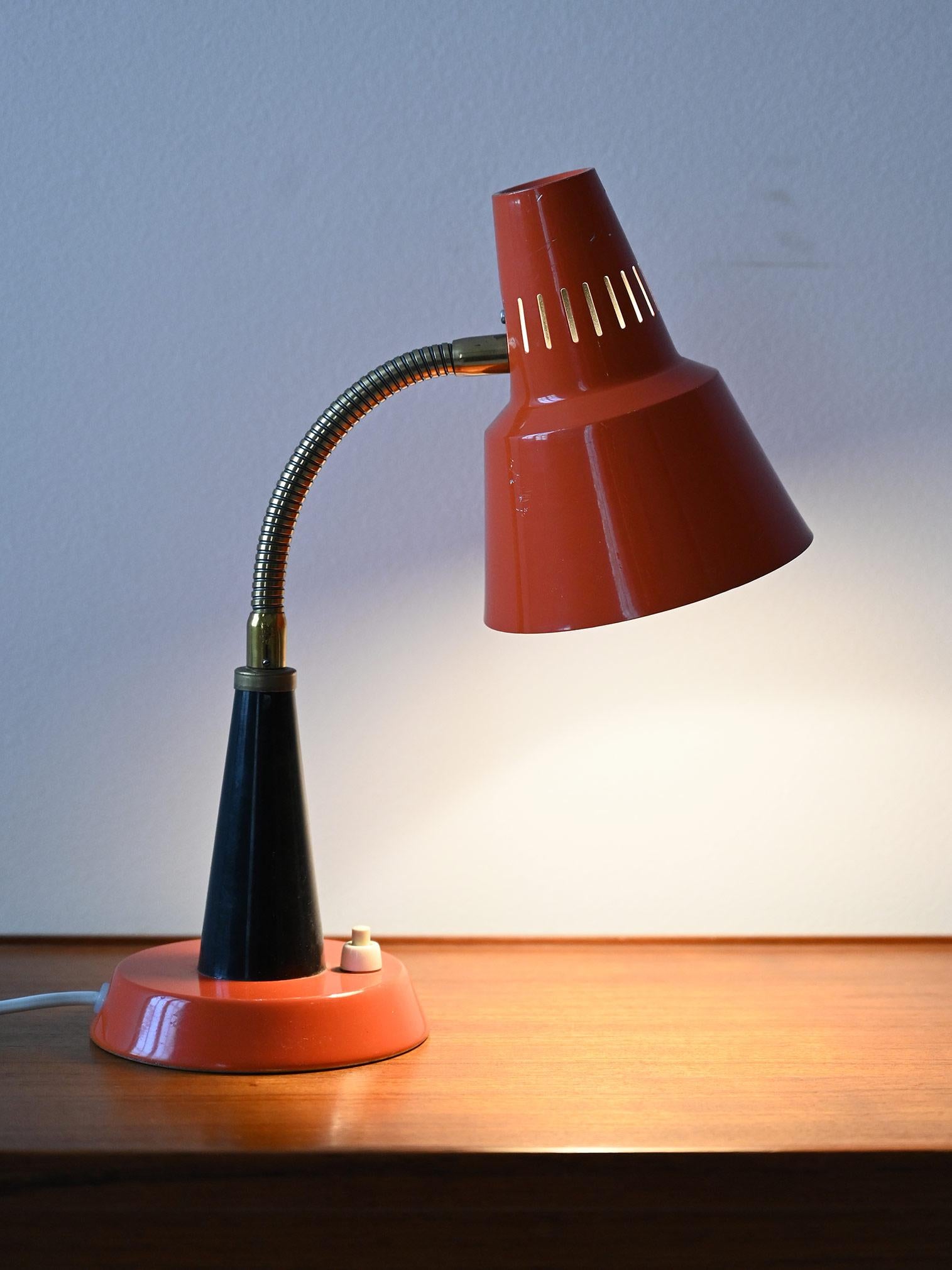A vintage table lamp with a distinctive 1960s design, it is distinguished by its vibrant orange color and conical metal shade. The flexible brass arm allows the direction of the light to be adjusted, adding practicality to the design.

The lampshade